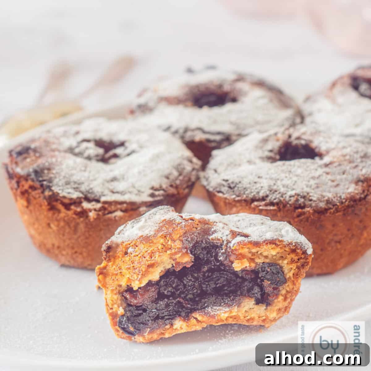 Decadent Hazelnut Mince Pies 10 A square picture with fruit mince pies on a white plate. One is in half and you can see the fruit mince filling.