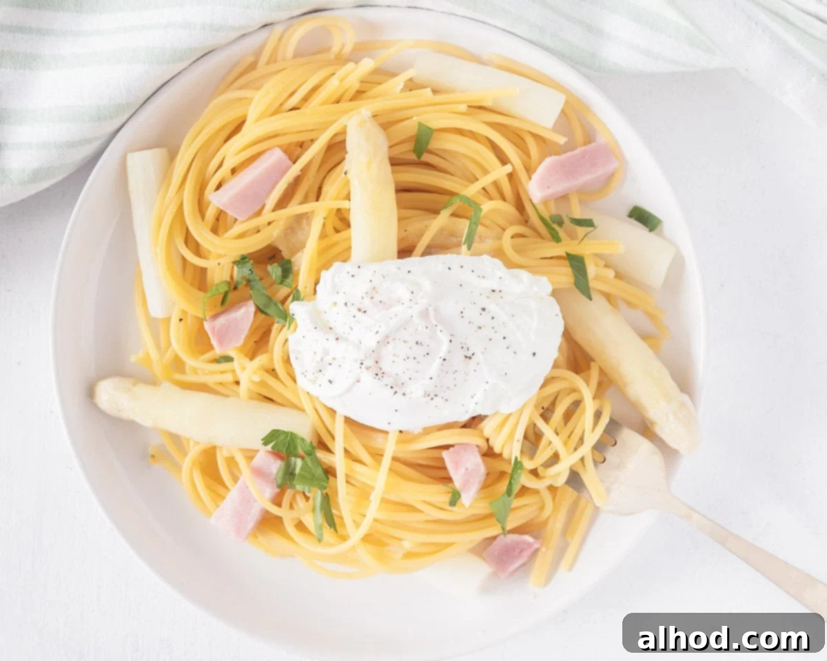 Effortless Asparagus Pasta with Poached Egg 7 A plate with spaghetti, poached egg, fresh parsley, ham, and asparagus, ready to be enjoyed.