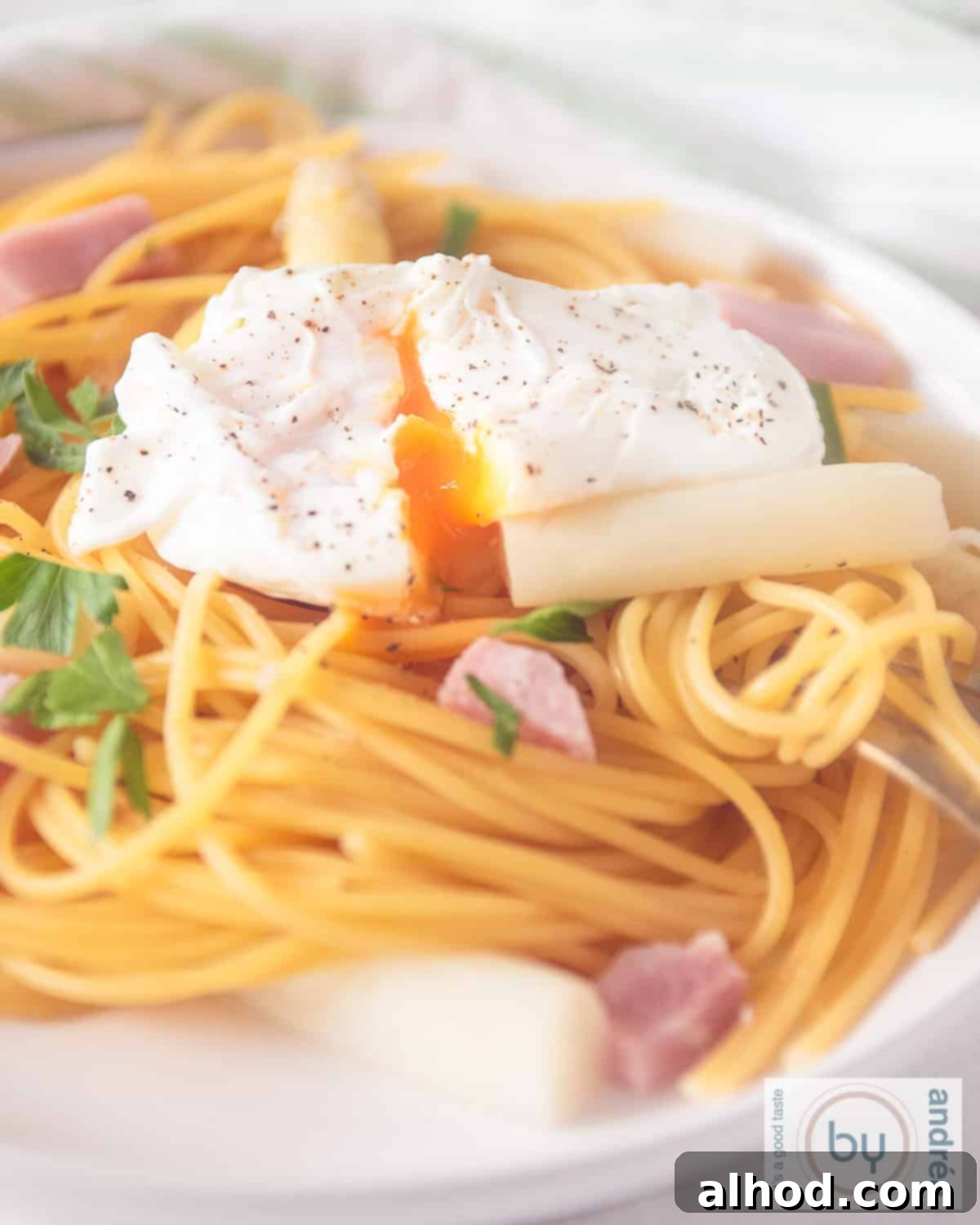 Effortless Asparagus Pasta with Poached Egg 8 A height picture: part of a white plate with asparagus, pasta, ham and poached egg, showing the creamy texture.