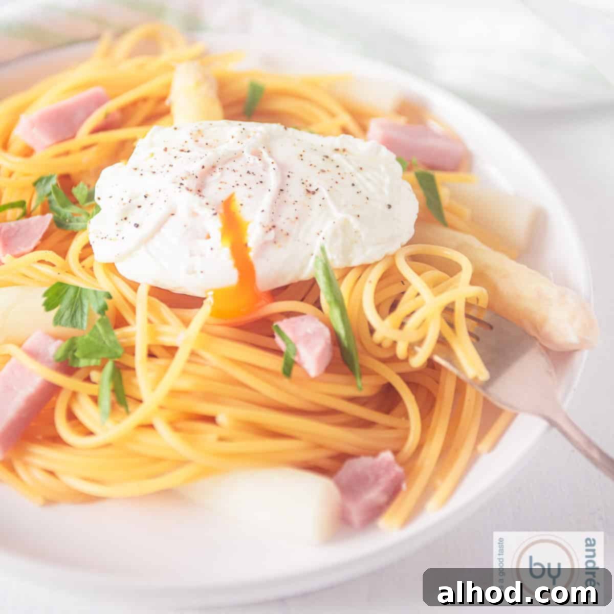 Effortless Asparagus Pasta with Poached Egg 9 A square picture of a white plate with spaghetti, ham asparagus and poached egg, garnished with fresh herbs.