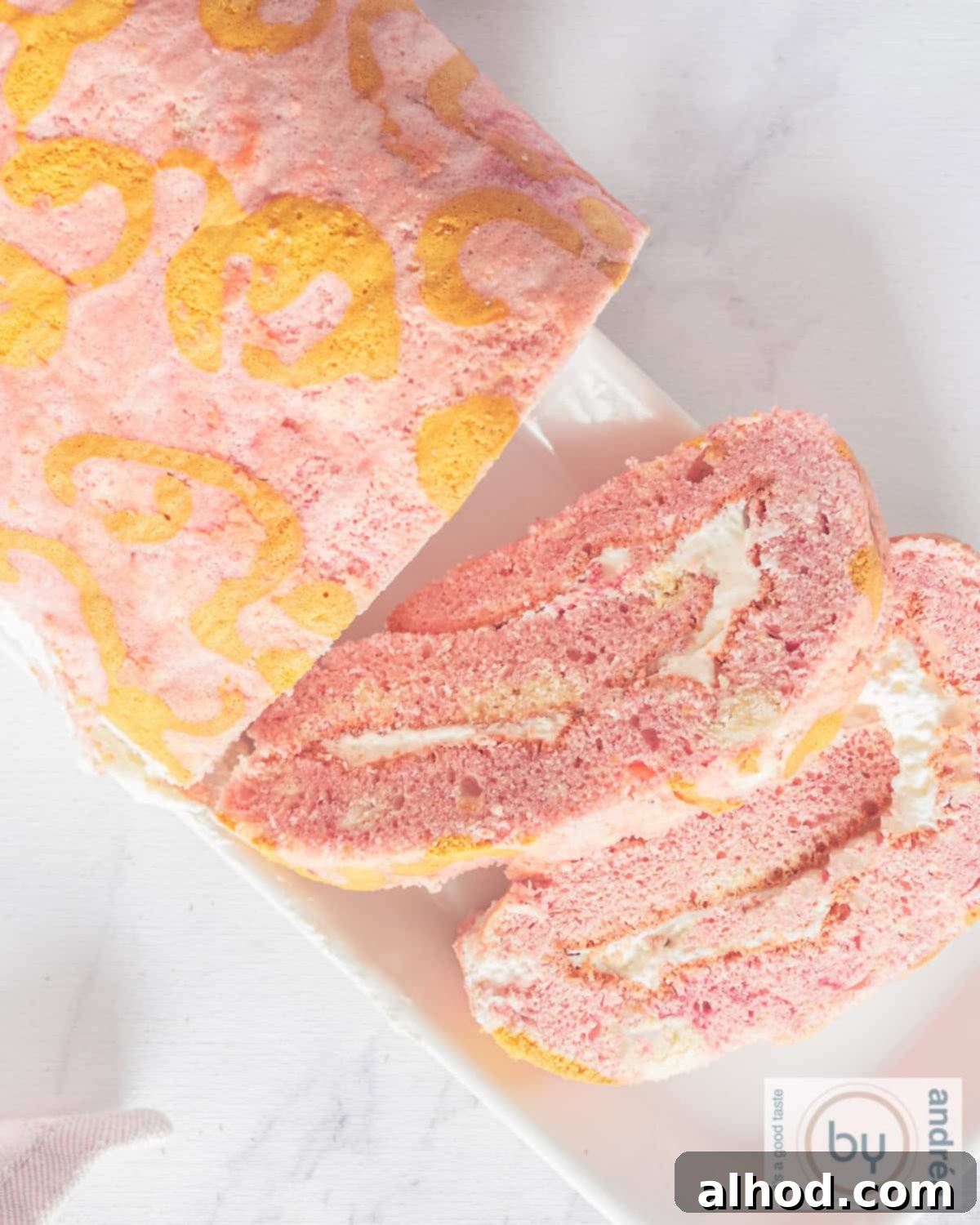 A vibrant pink Swiss roll cake with intricate golden swirls on its surface, presented beautifully against a clean white background.