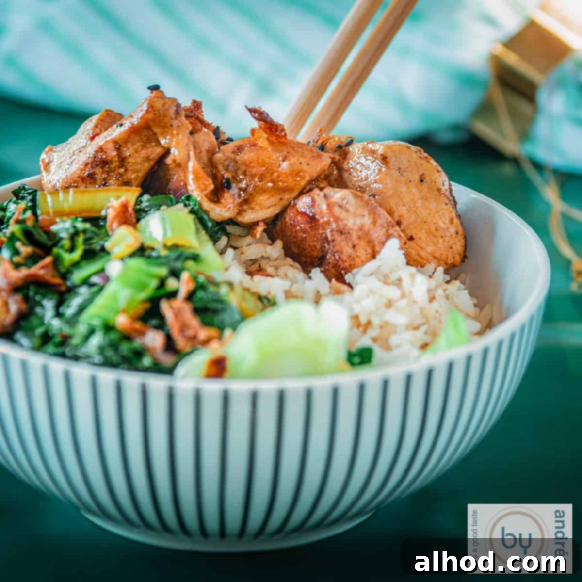 A square photo with a white striped bowl containing bok choy, rice and sticky ketjap chicken.