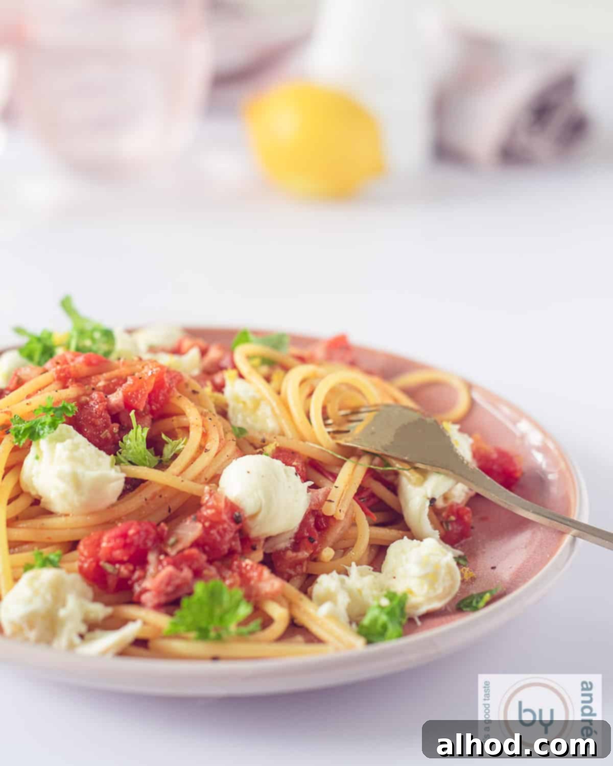 Savory Bacon, Tomato, and Mozzarella Spaghetti 3 A height photo with a pink plate filled with pasta, mozzarella, bacon and parsley. A fork is on the plate.