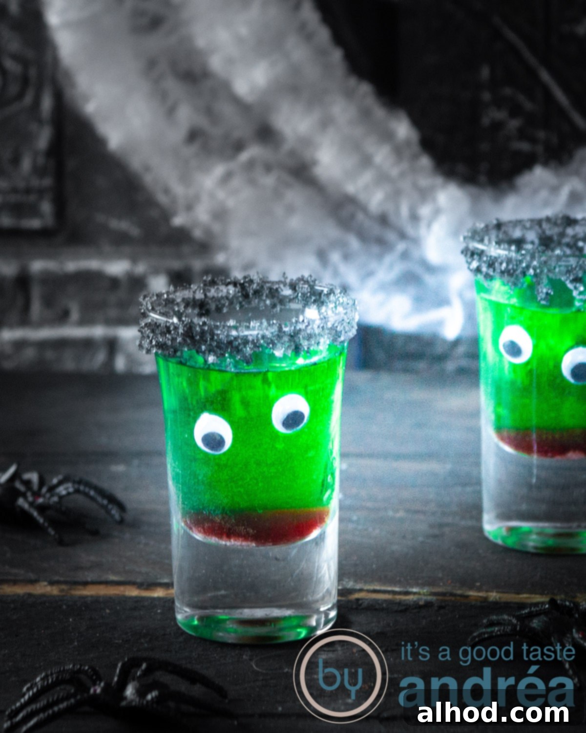 Kid-Friendly Halloween Potions 2 A two-layered Halloween mocktail in a shot glass with edible eyes and a black sugar rim, set against a dark background.