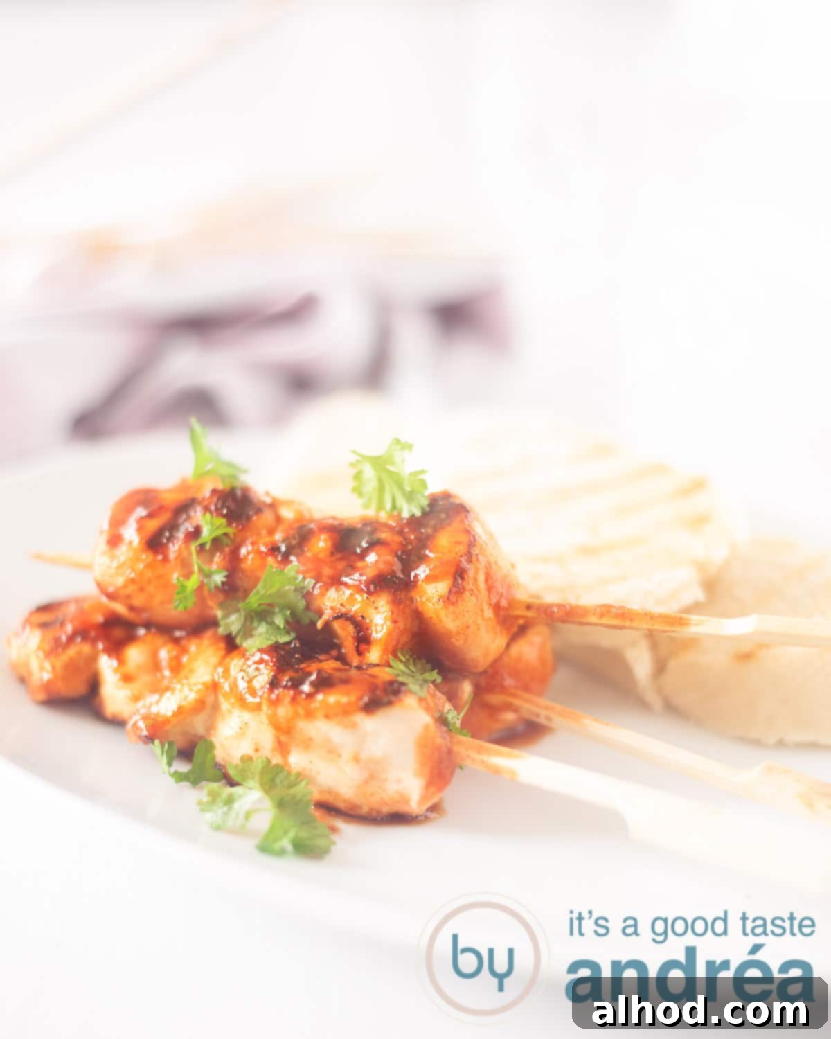 Bourbon Glazed Chicken and Bacon Skewers 3 An elevation photo with a white plate, 3 skewers marinated with chicken and some slices of baguette