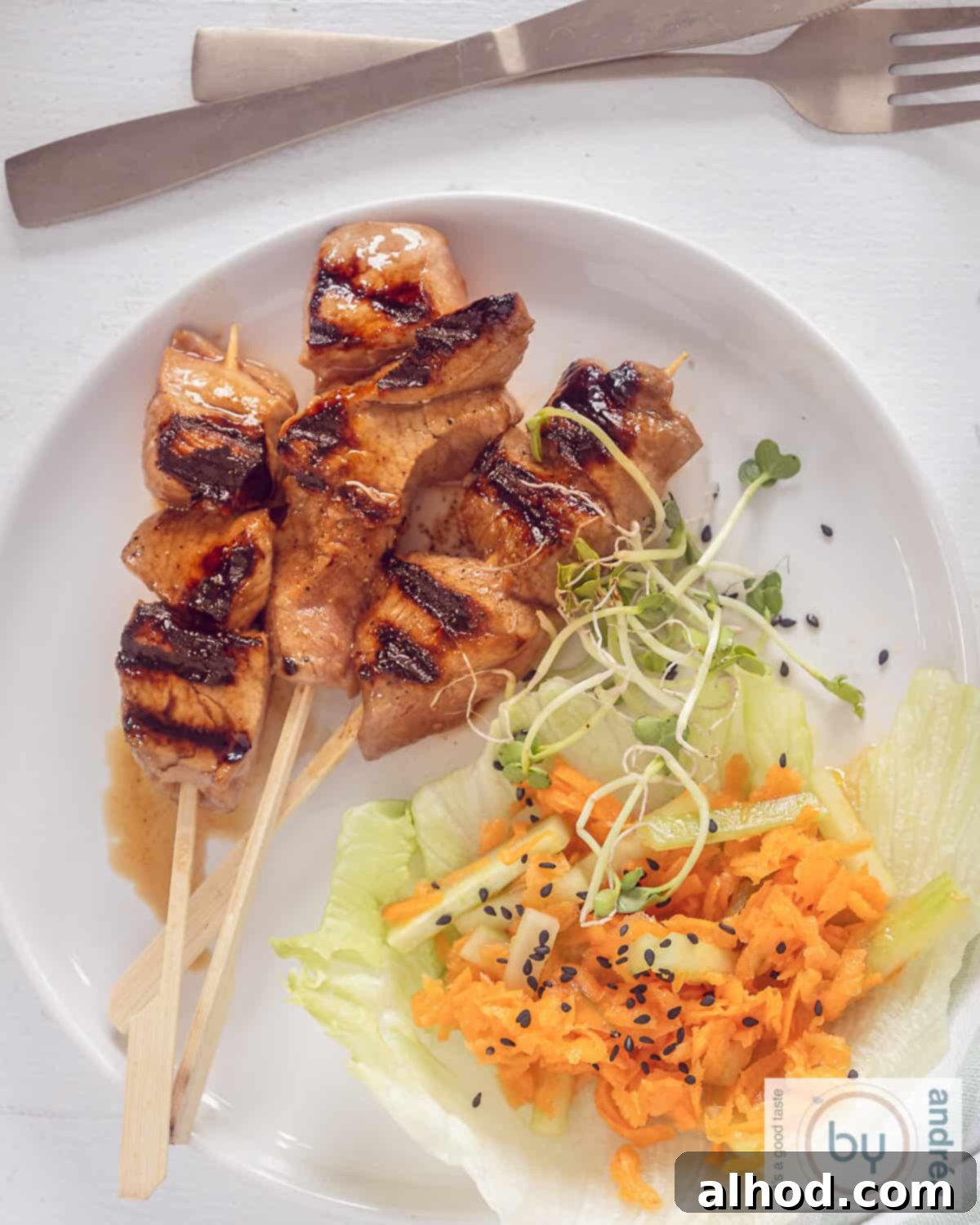 Sweet & Savory Asian Skewers with a Cooling Veggie Salad 3 A photo from above of a white plate with three oriental pork tenderloin skewers on the left and a cucumber and carrot salad on the right.