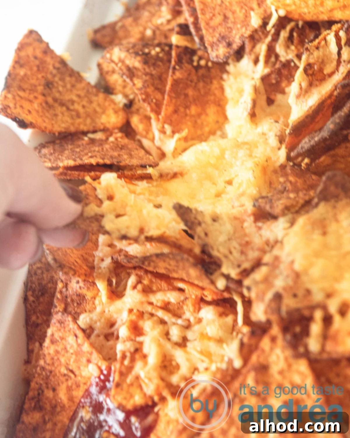 Loaded Nacho Beef Bake 2 a part of a Mexican nacho casserole. A hand is taking a cheesy nacho cheese tortilla chips.