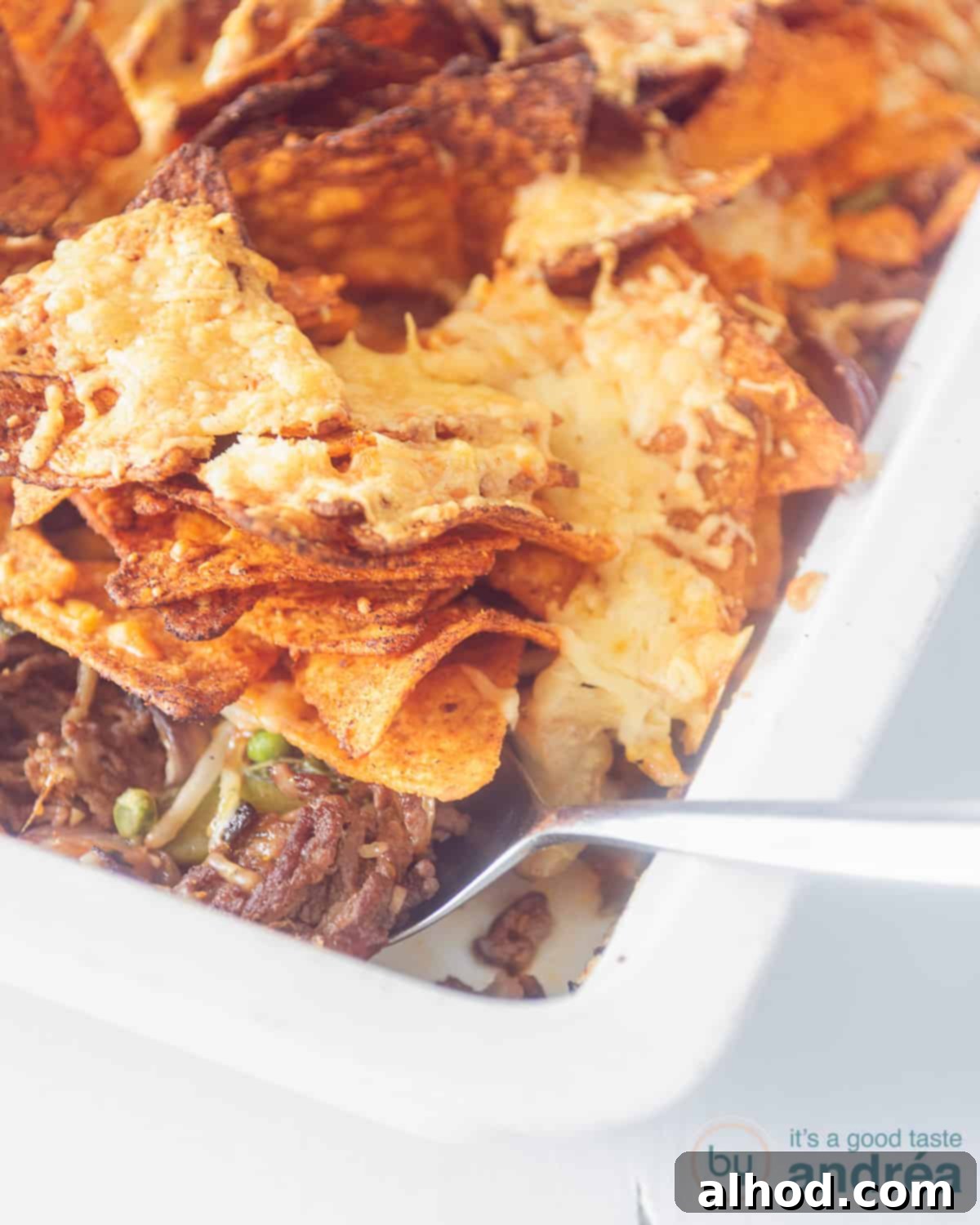 Loaded Nacho Beef Bake 3 An overhead photo with a white baking dish with nacho dish lifting some nachos up. Includes minced meat and vegetables.
