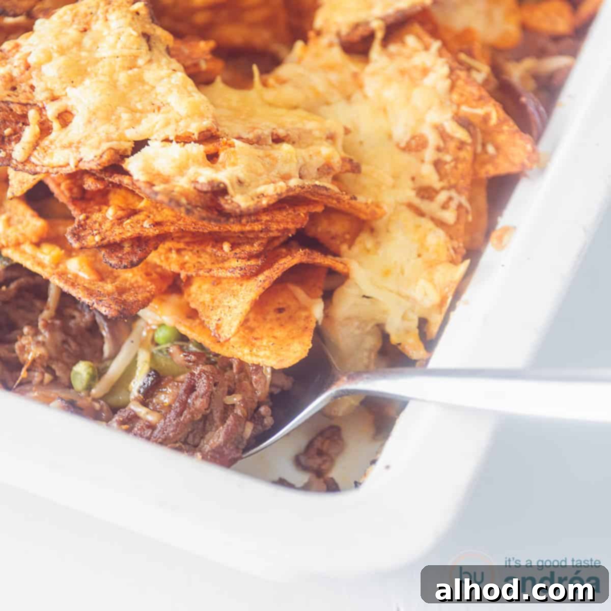 Loaded Nacho Beef Bake 4 A square photo with a white baking dish with minced meat and vegetable filling (part of it can be seen) with nachos gratinated on top