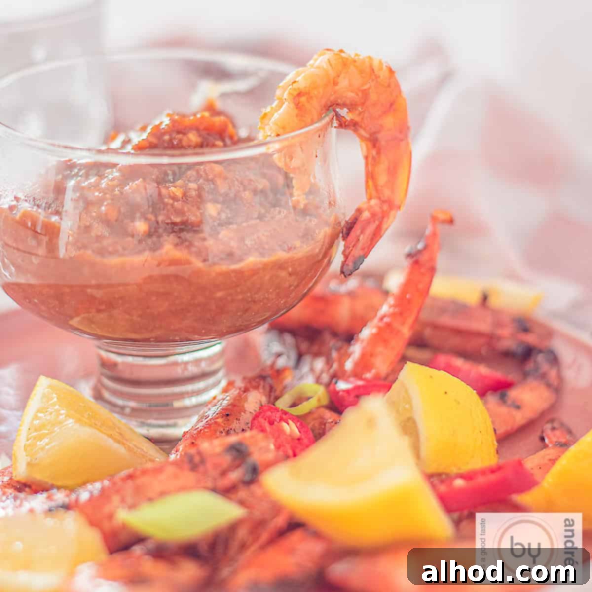Sizzling Summer Satay Shrimp 4 A square photo with a glass filled with cashew satay sauce and grilled shrimps, spring onion, lemon and peppers surrounding it, ready for serving.