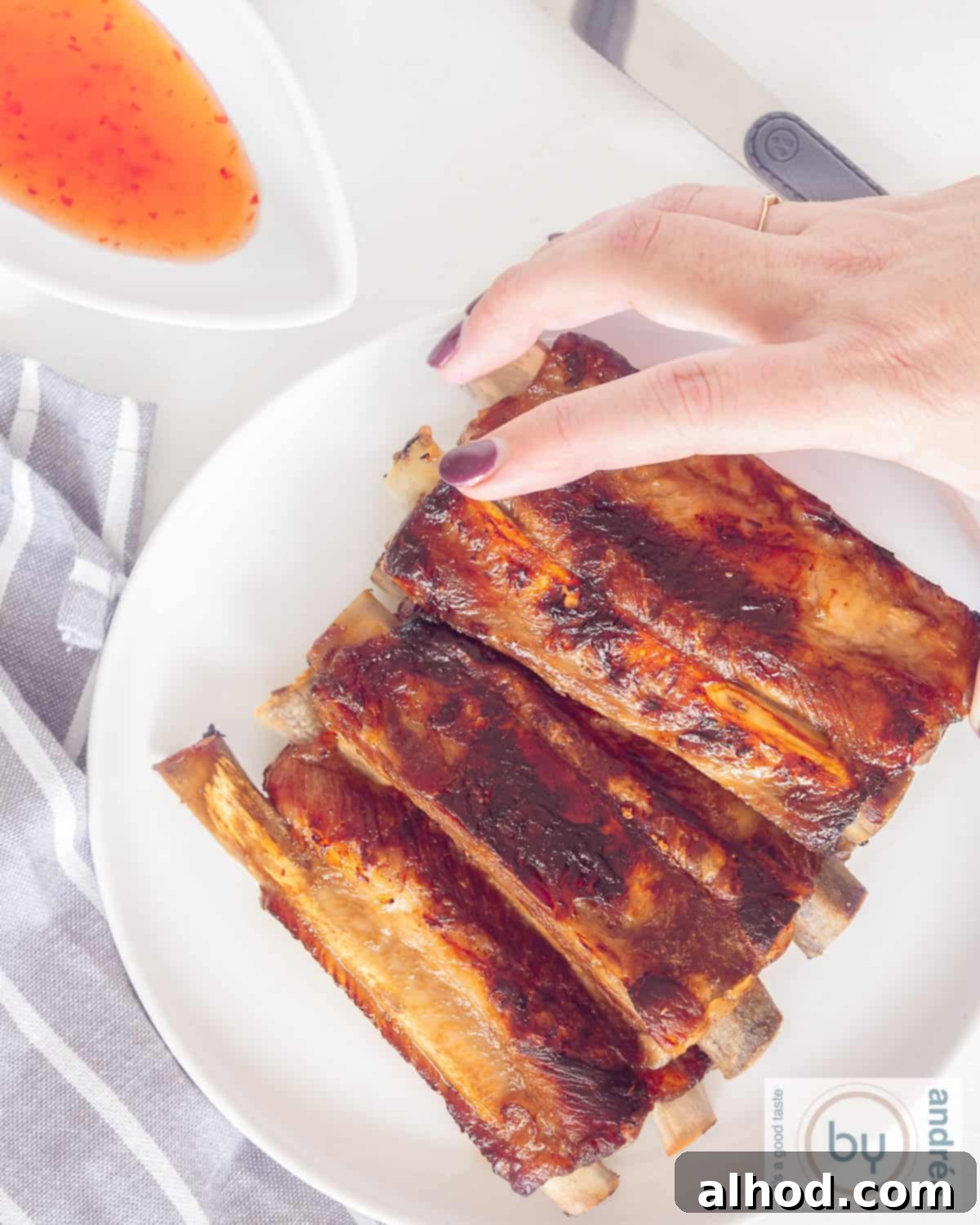 Caramelized Bourbon Soy Ribs 3 An overhead shot of a plate of ribs. A hand grasps a sticky rib, showcasing its tenderness and glazed finish.