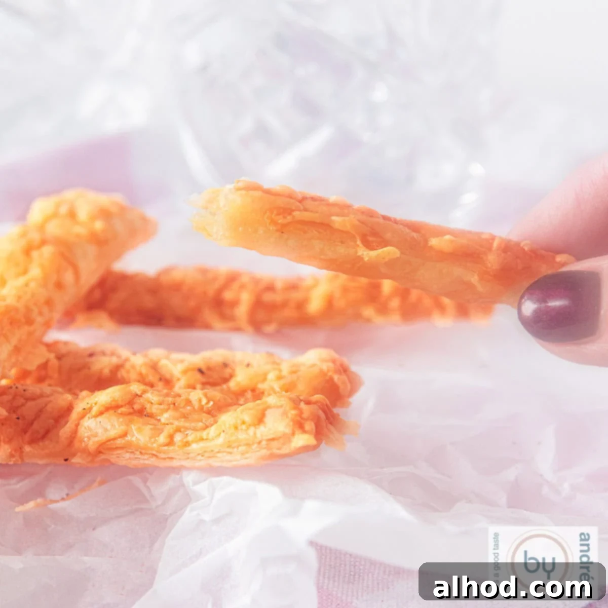 Easy 3 Ingredient Parmesan Puff Pastry Sticks 4 A square photo with a baking sheet with cheese sticks, half of which is being held.