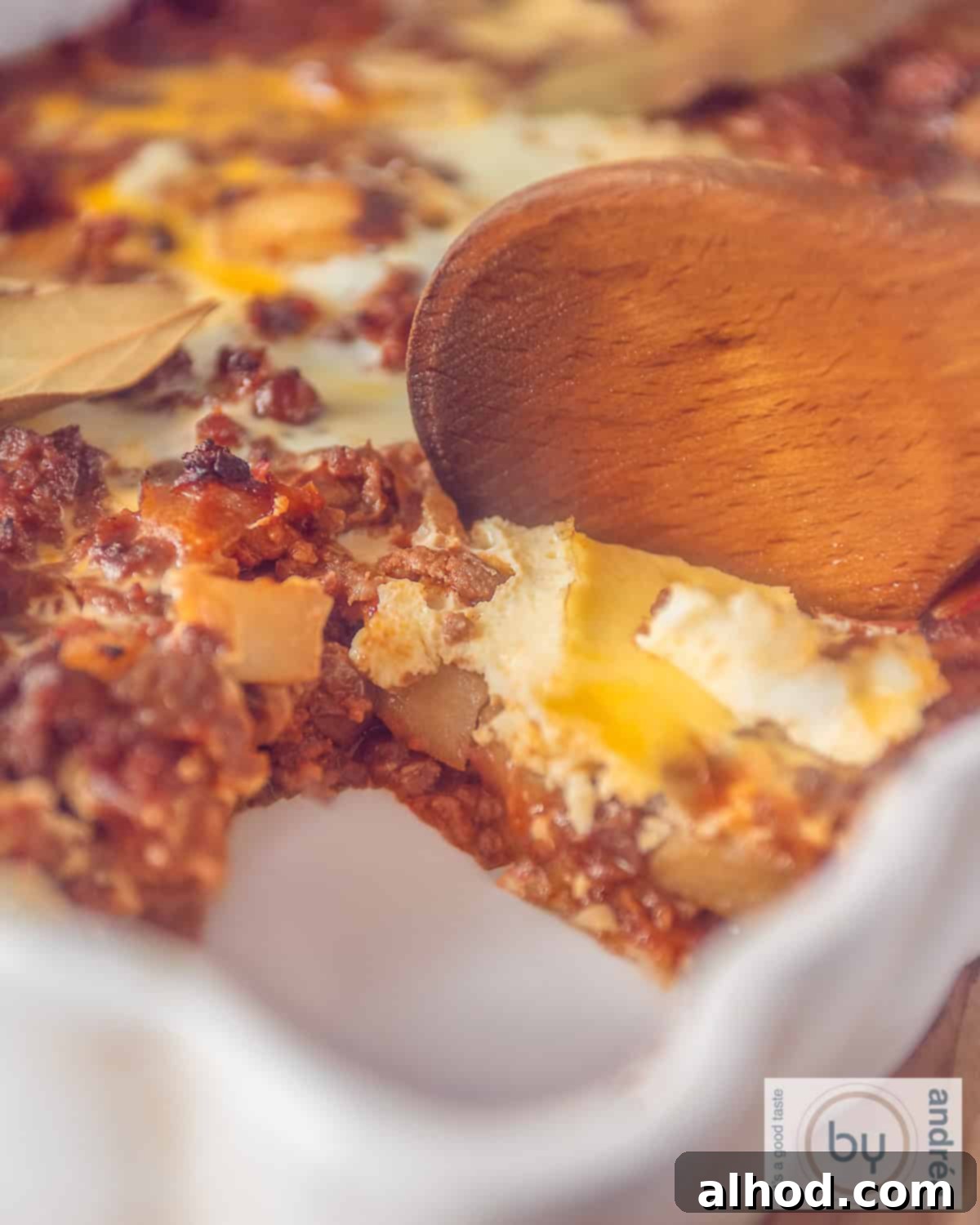 Classic South African Bobotie Beef with Sweet Fruit 3 A portion of a bobotie casserole dish with a scoop removed. A wooden spoon is stuck inside.