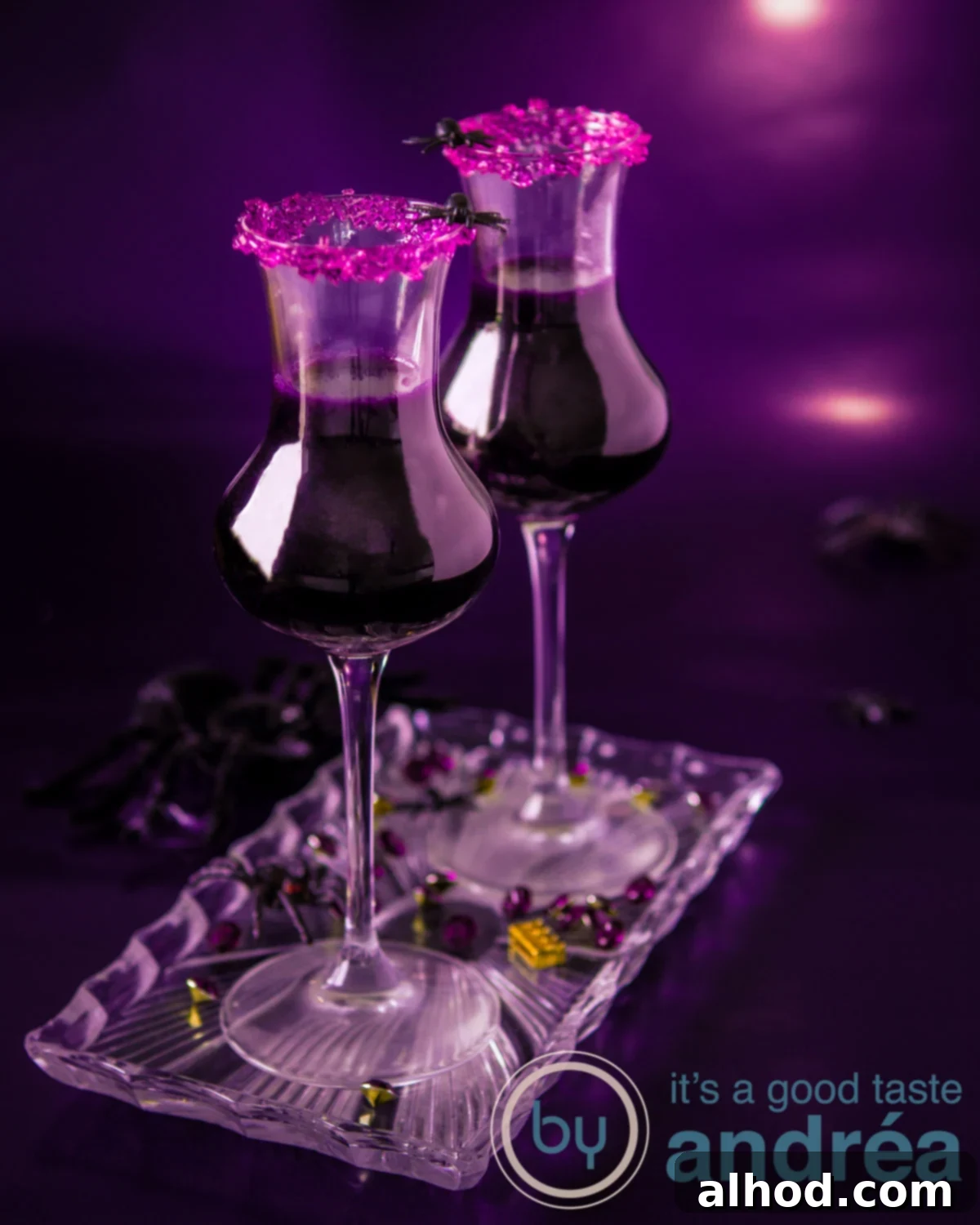 Two cocktail glasses filled with a vibrant purple Halloween witch potion cocktail, adorned with a sparkling purple sugar rim, against a dark, mysterious background.