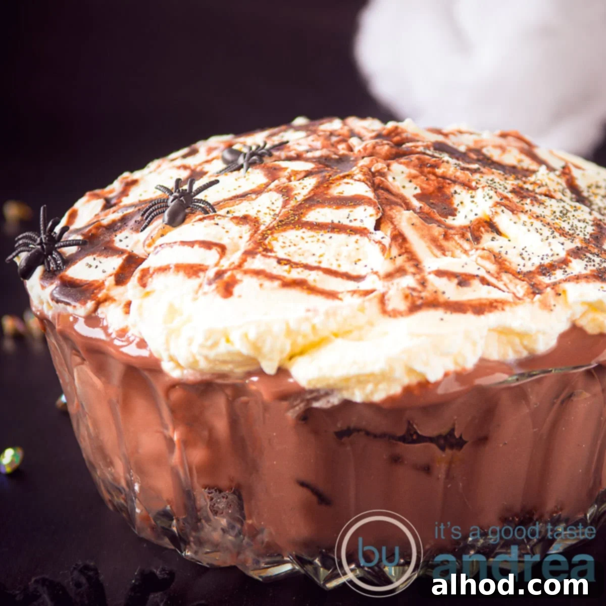Oreo Brownie Graveyard Trifle 5 A square photo showing part of a glass bowl filled with oreos, brownies, chocolate custard and whipped cream. On top of a caramel spider web with spiders, ready for Halloween.