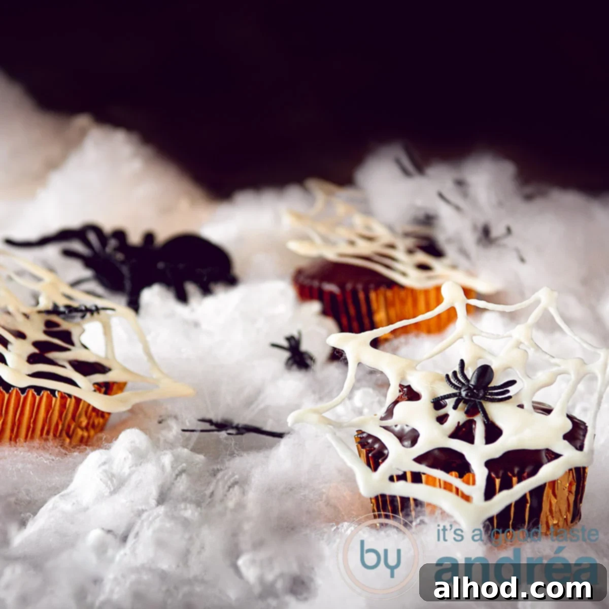 Spooky Nutella Chocolate Spiderweb Cupcakes 4 a square photo of nutella cupcakes with white chocolate spiderwebs on a white cloudy ground.