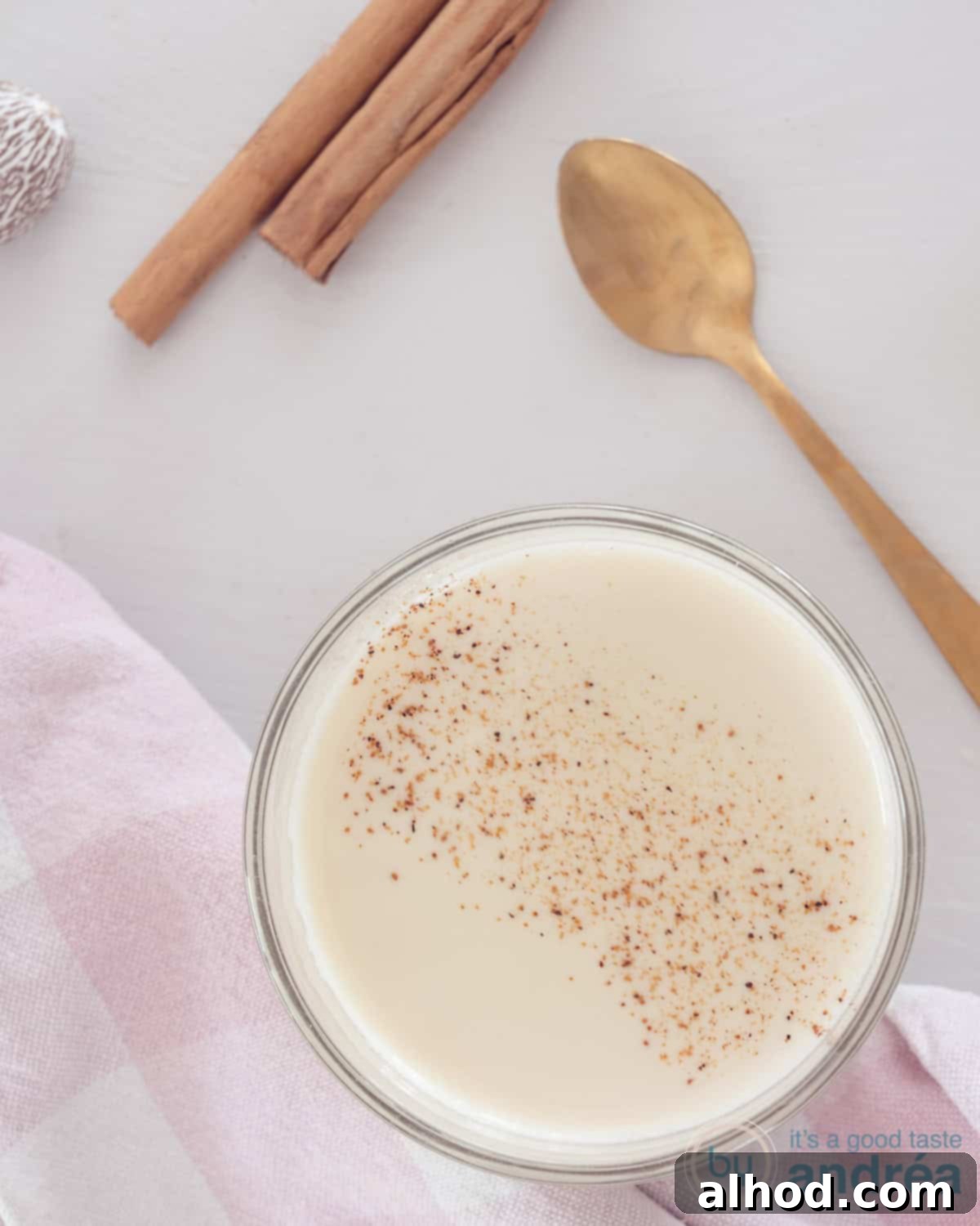 DIY Spiced Chai Perfection 2 A glass filled with chai tea on a white background, surrounded by a golden teaspoon, cinnamon sticks, and nutmeg.