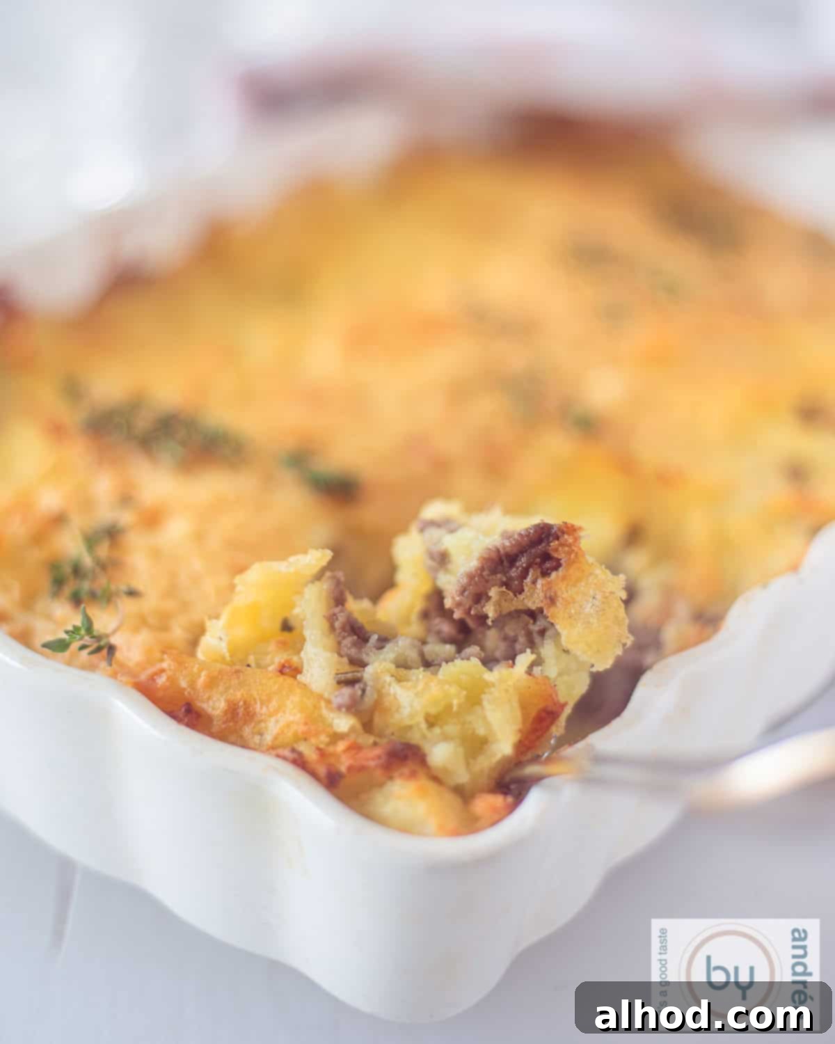 Hearty Beef and Potato Comfort Bake 2 A height picture with a white casserole mashed potato, ground beef gratin. A spoon is taking a scoop.