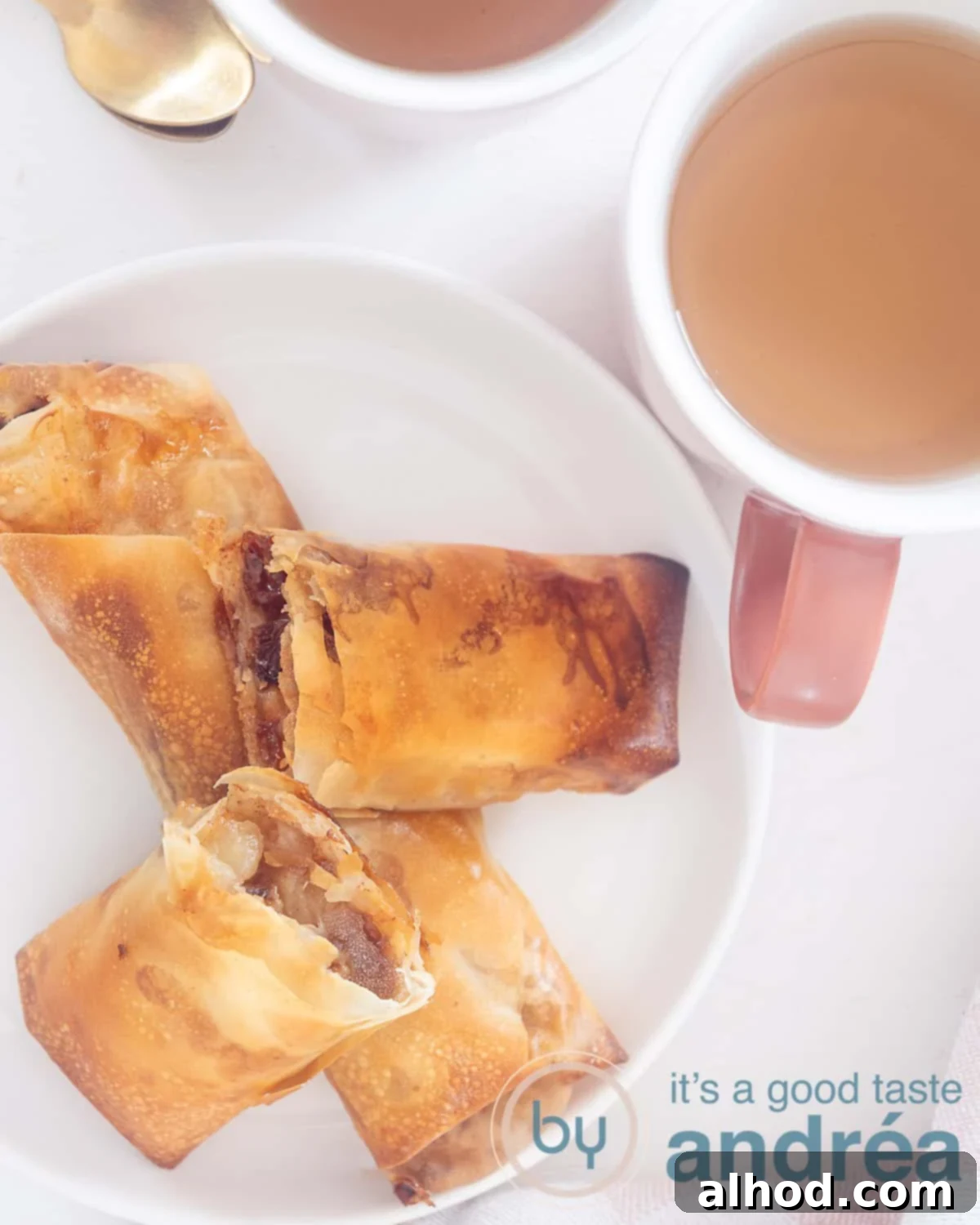 A photo from above showing a white plate with one whole and two halves of filo pastry apple turnover on a white plate. Two cups of tea upstairs.