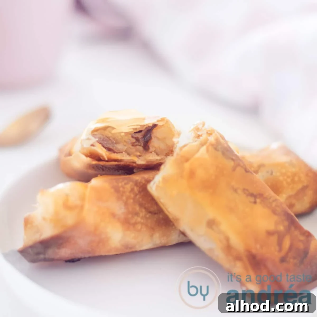 A square photograph of a white plate with a filo pastry apple turnover and two halves on top. The filling is visible.