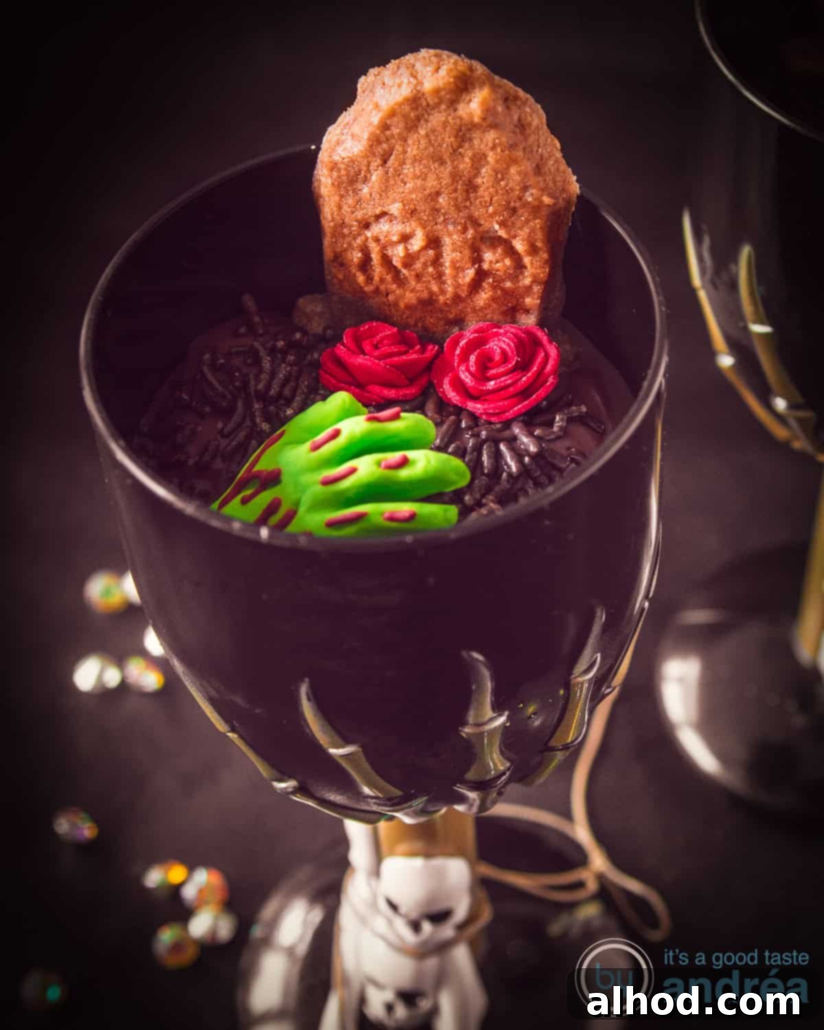 A black glass filled with luscious chocolate mousse, adorned with a playfully spooky zombie hand, a gingerbread tombstone cookie, and delicate sugar roses, all set against a mysterious black background, perfect for a Halloween celebration.