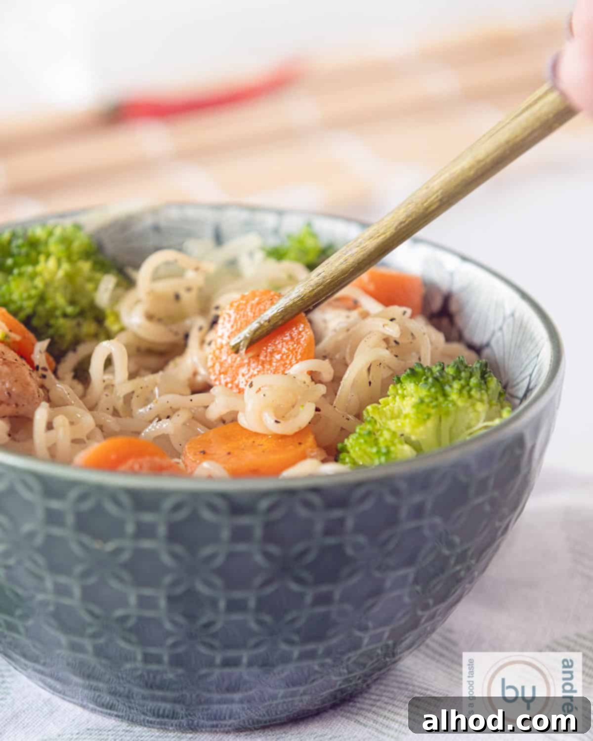 Speedy Chicken Noodle Stir-Fry with Garden-Fresh Veggies 2 A vibrant green bowl brimming with stir-fried chicken, crisp broccoli florets, and thinly sliced carrots. Two chopsticks are poised, gently lifting a piece of carrot from the fragrant dish.