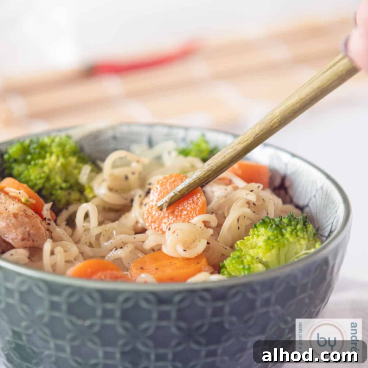 Speedy Chicken Noodle Stir-Fry with Garden-Fresh Veggies 8 A square picture with a green bowl filled with noodles, carrots broccoli and chicken. Chopsticks taking a carrot.