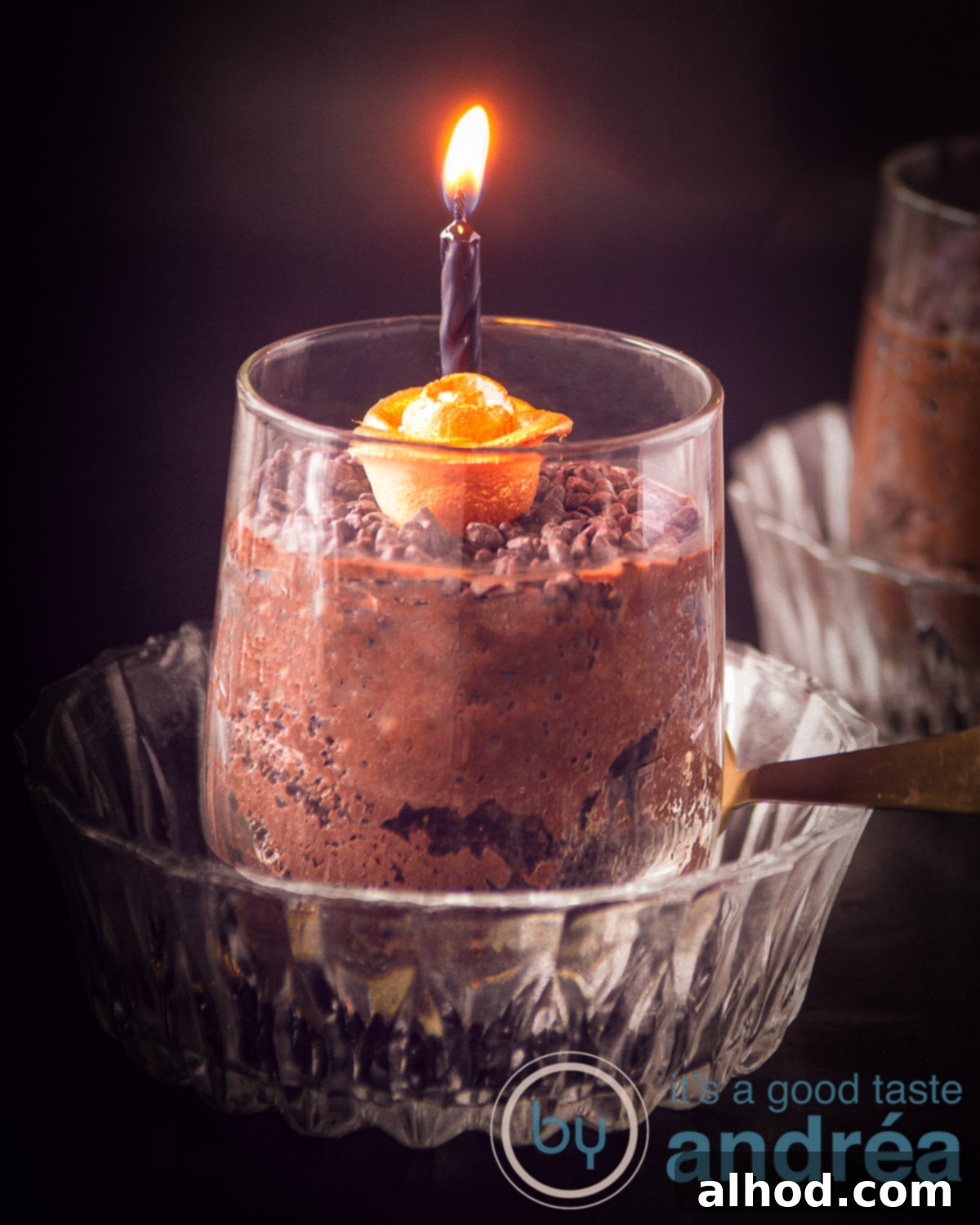 Spooktacular Chocolate Mousse 2 A glass bowl with a glass in it filled with mousse of chocolate. topped with a golden rose and a lit black candle on a black background