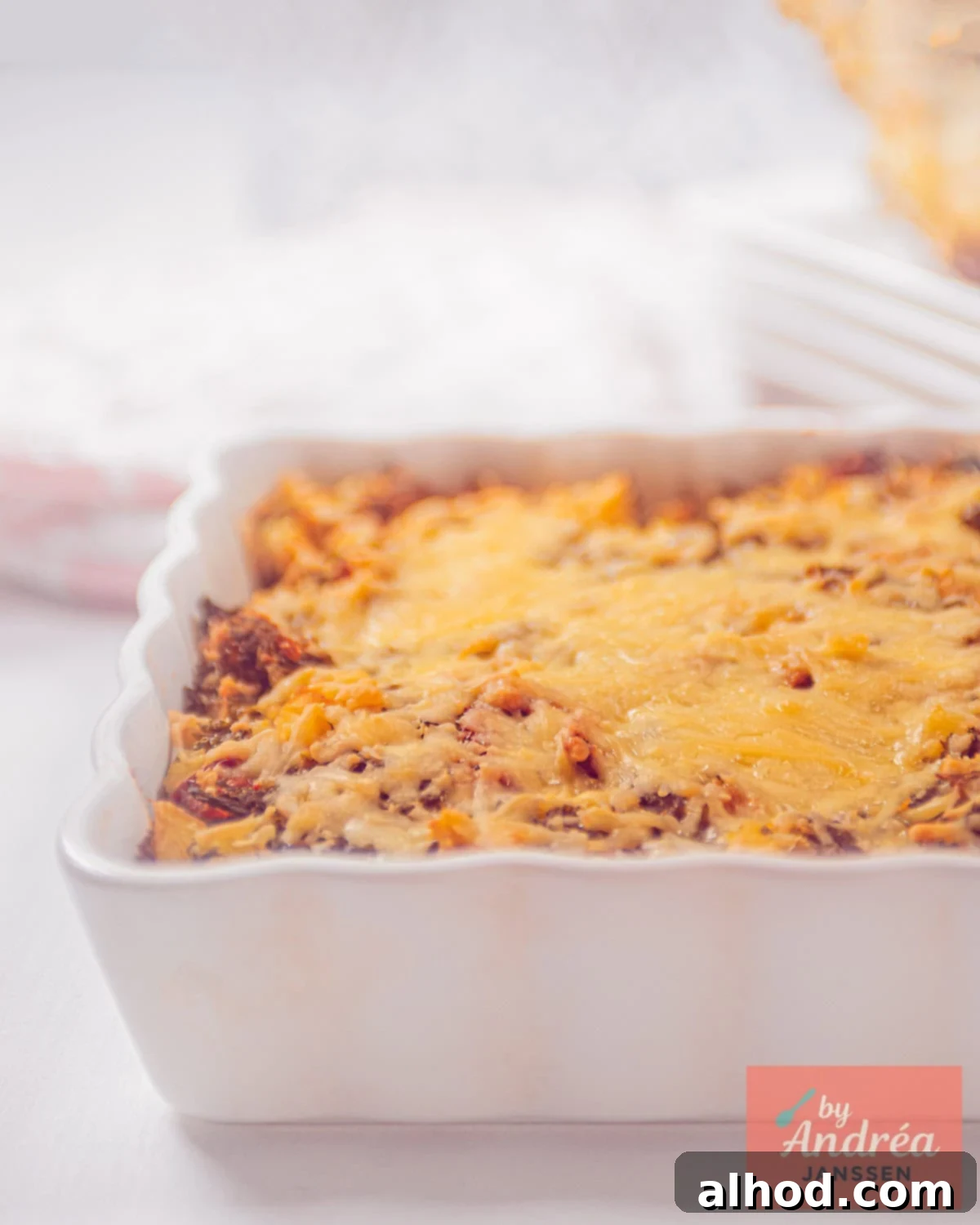 A portion of a white oven dish with a mashed kale with tomato and cheese, gratinated.