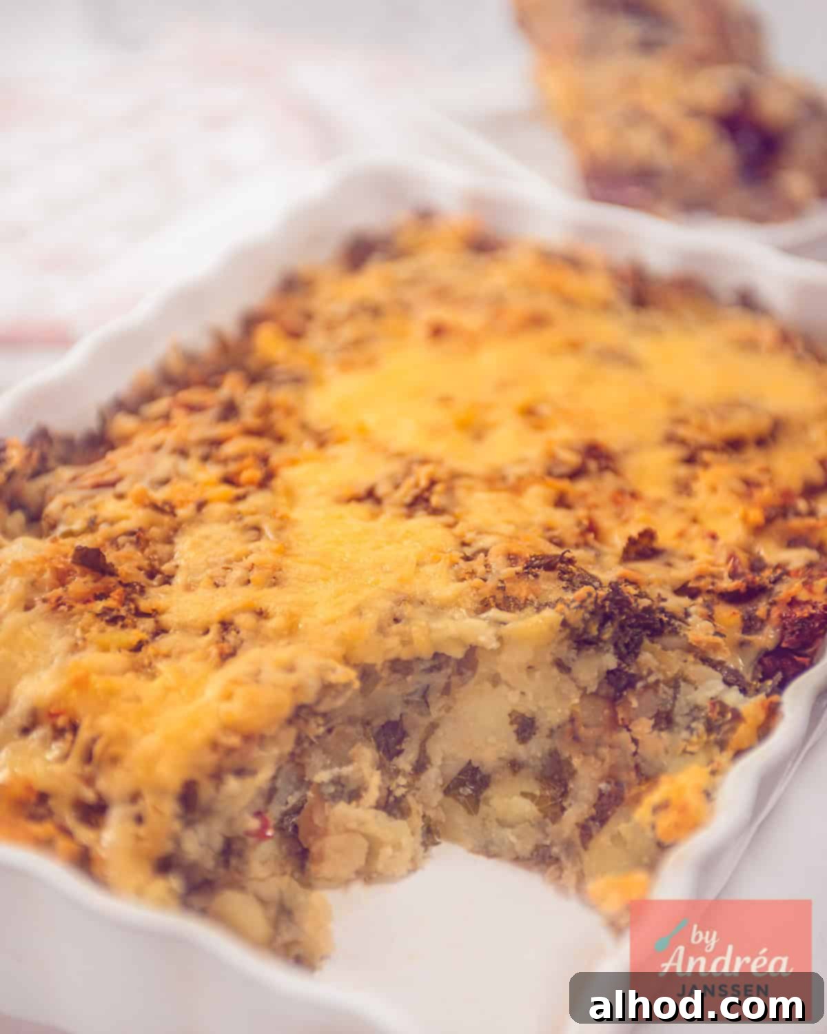 Hearty Kale and Potato Bake 5 A white oven dish with a kale mash with sun-dried tomatoes under a roof of melted cheese.