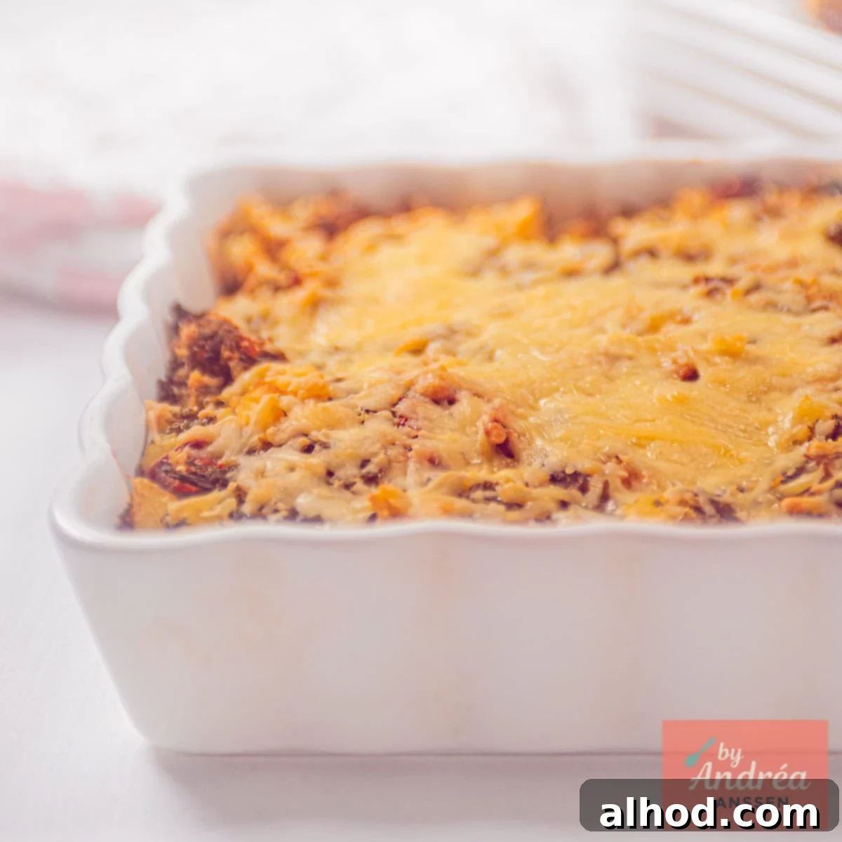 Hearty Kale and Potato Bake 6 A square photo showing part of a white baking dish filled with a gratin of kale mash, cheese, and tomato