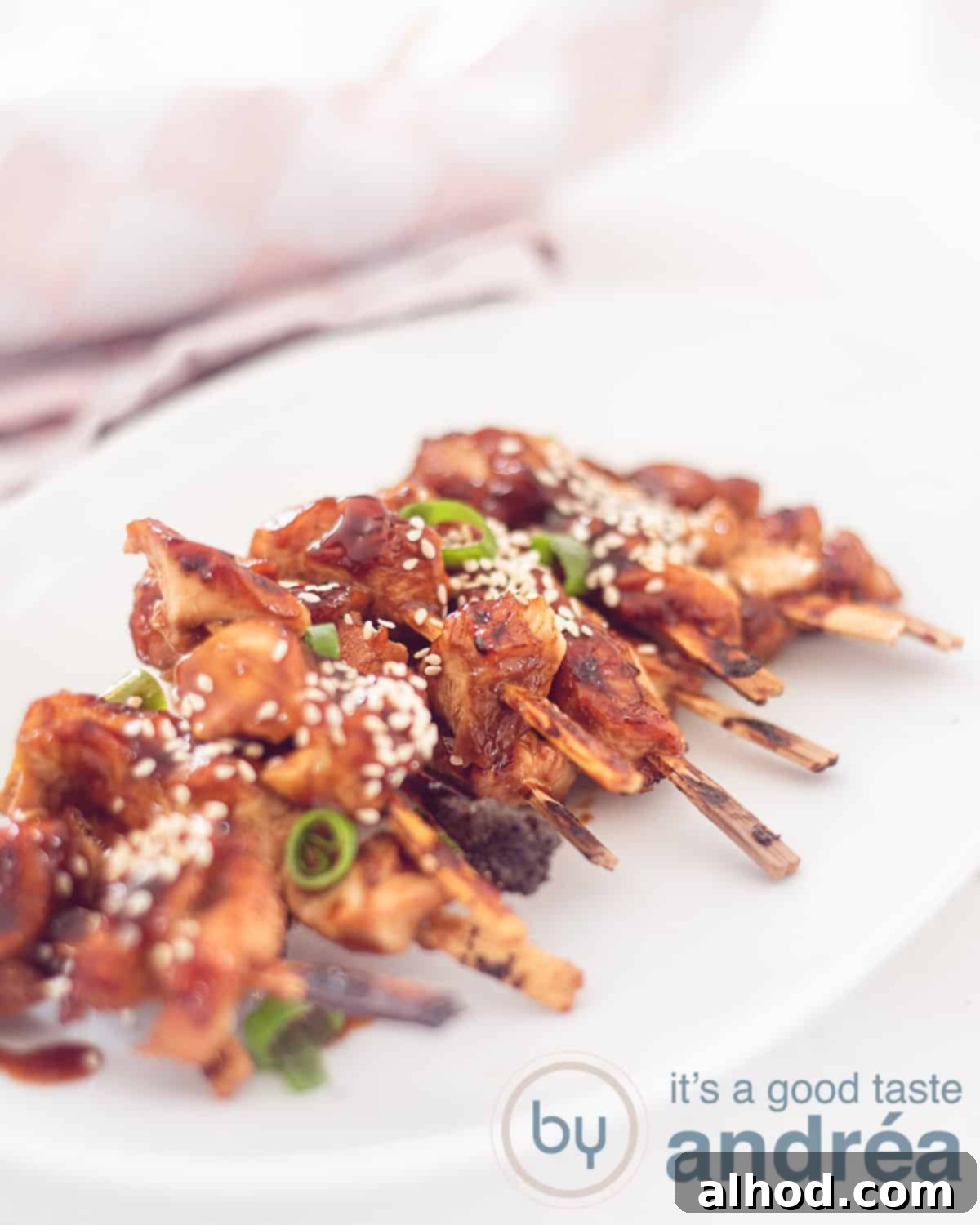 Authentic Japanese Chicken Yakitori 2 An elevation photo with a white plate on a white background with twenty chicken skewers Japanese style with sesame, yakitori sauce and spring onion.