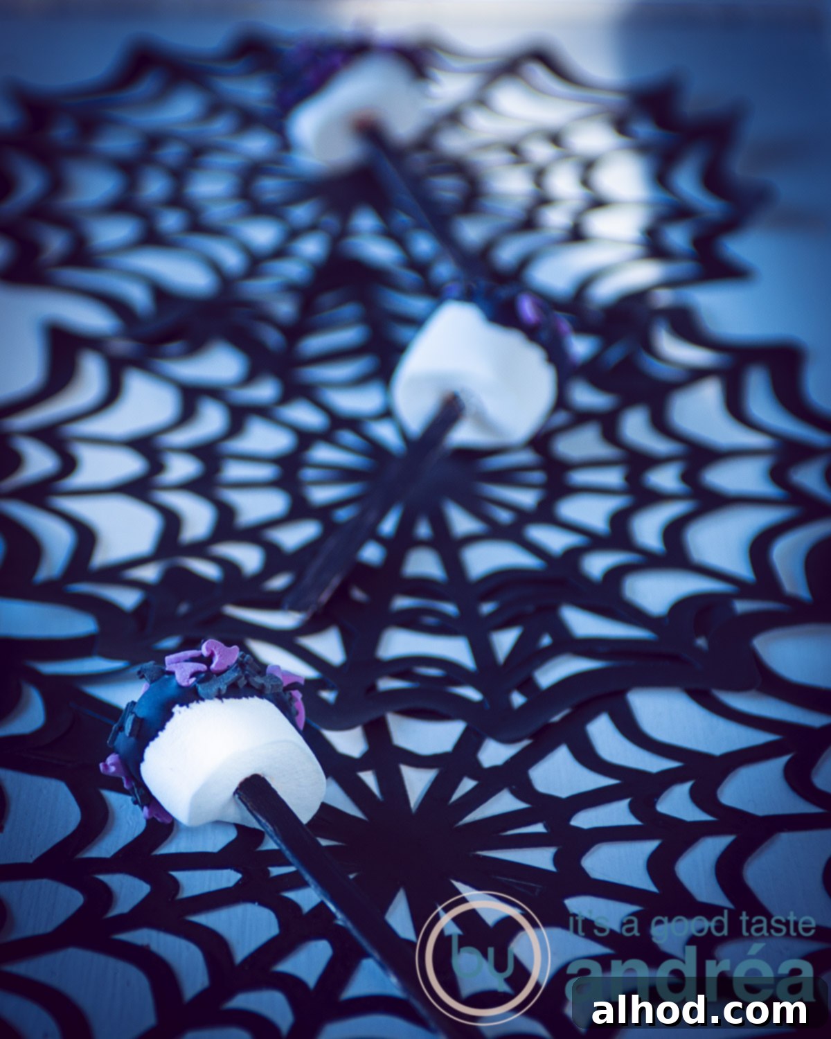 Ghoulishly Quick Marshmallow Sticks 3 three Halloween marshmallow pops vertically on spider cobs (black) on a blue background