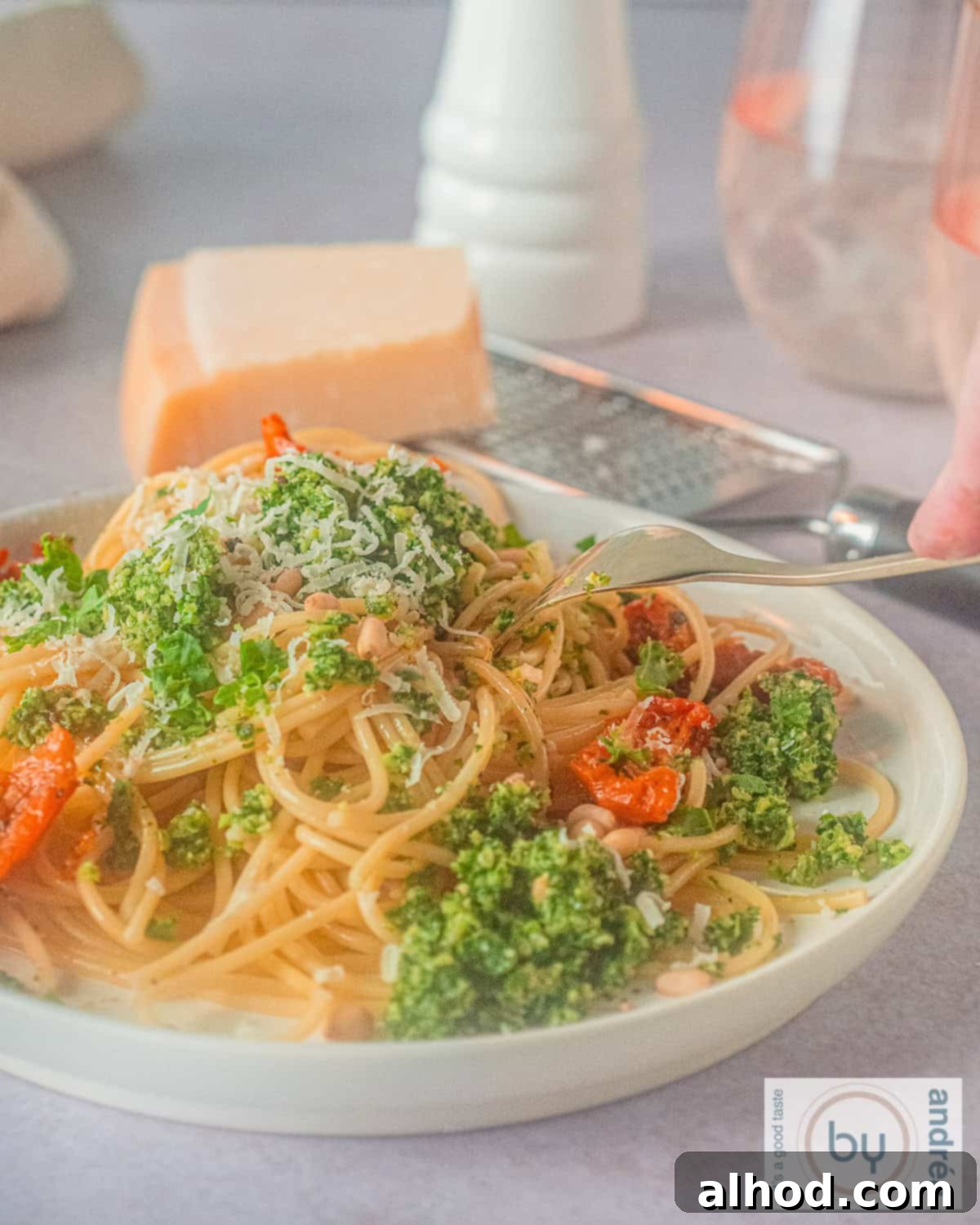 Vibrant Kale Pesto Pasta 2 A height photo of a plate full of spaghetti, sun-dried tomatoes, kale pesto and Parmesan cheese.