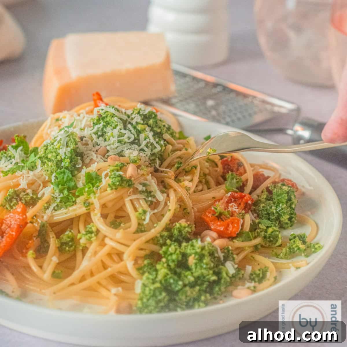 Vibrant Kale Pesto Pasta 6 A square photo of a white plate with spaghetti, kale pesto and sun-dried tomatoes. A fork is poking the plate.