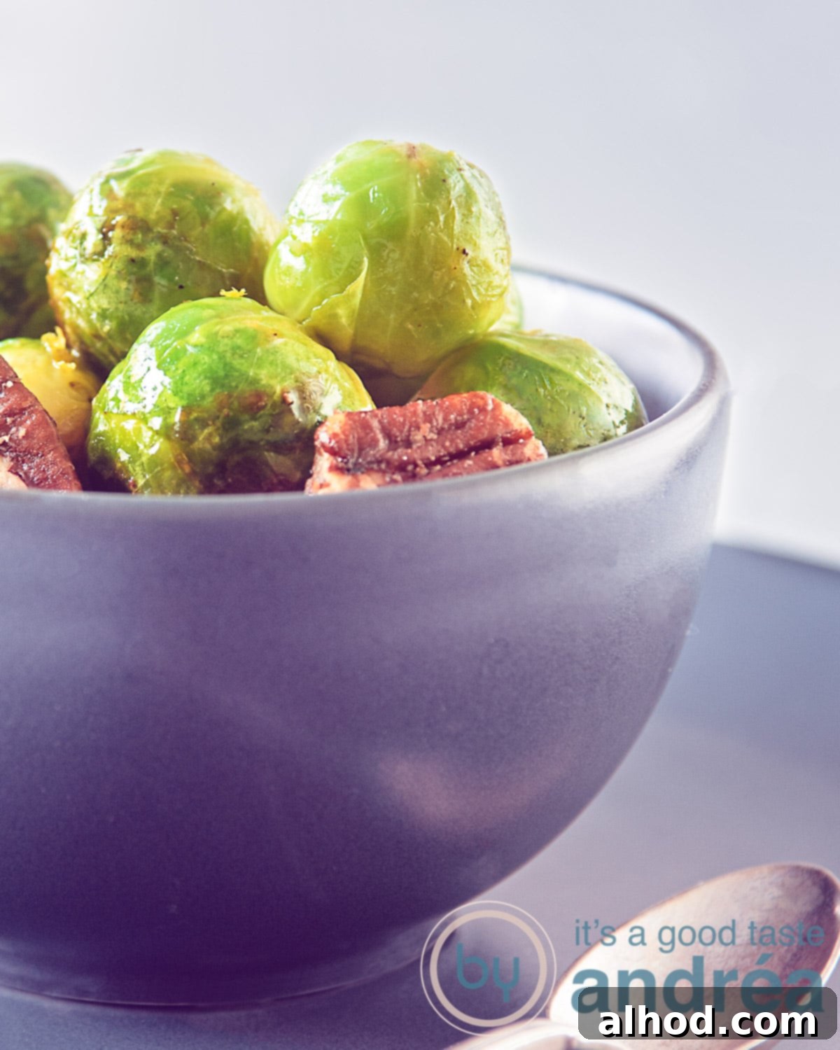 Zesty Orange Glazed Brussels Sprouts 2 A beautiful presentation of stir-fried Brussels sprouts adorned with a glistening orange balsamic glaze and scattered pecans, served in a stylish gray dish on a dark background.