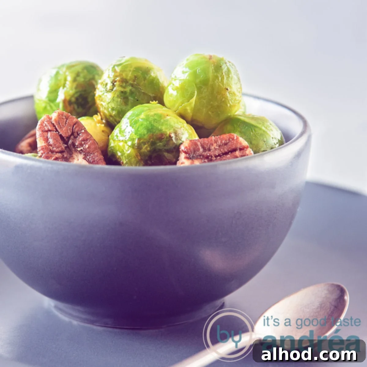 Zesty Orange Brussels Sprouts 6 A square photo with a gray bowl filled with Brussels sprouts, pecan and delicious orange glaze. A dark gray background. A spoon in the front.