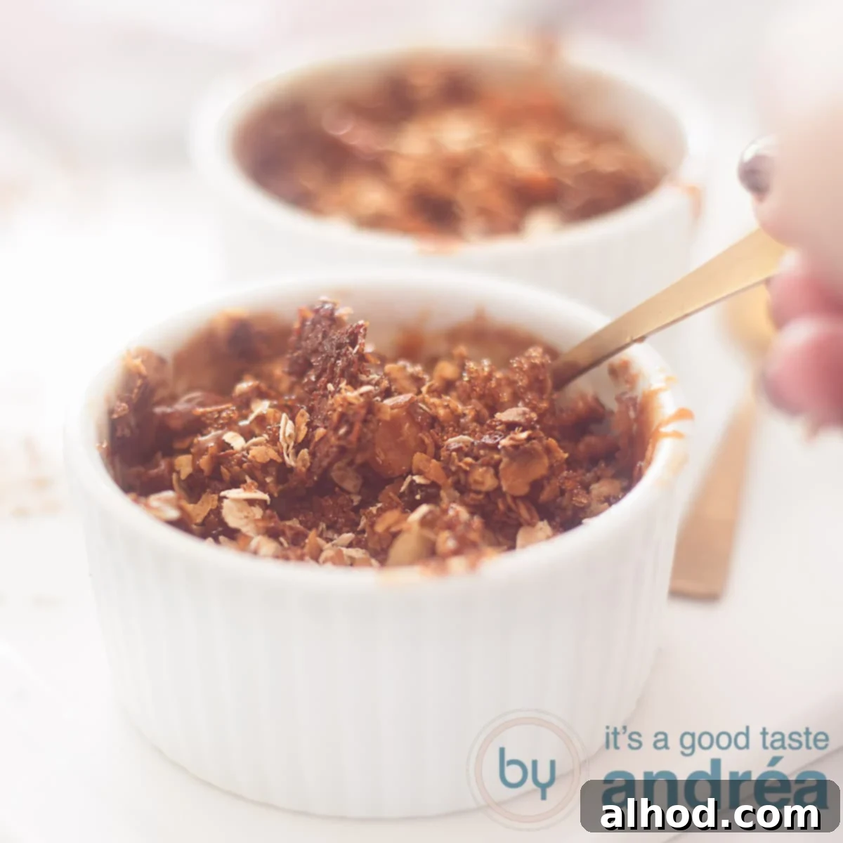A square photo of two ramekins filled with apple pie granola. A hand takes out a spoon.
