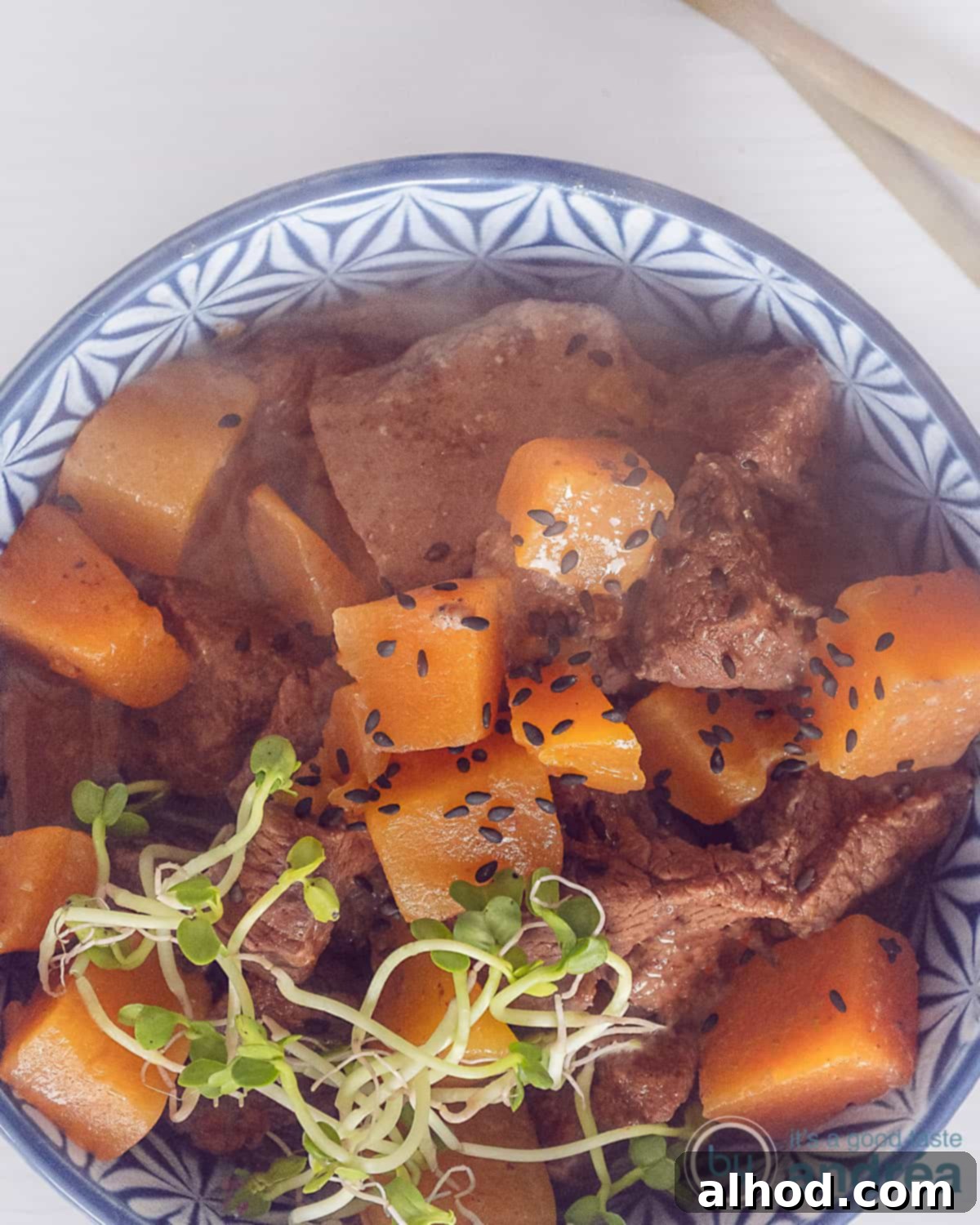 Speedy Rich Beef and Pumpkin Curry 2 A height photo with a photo from above of a blue bowl of pumpkin and steak curry on a white background. Two golden chopsticks at the top right