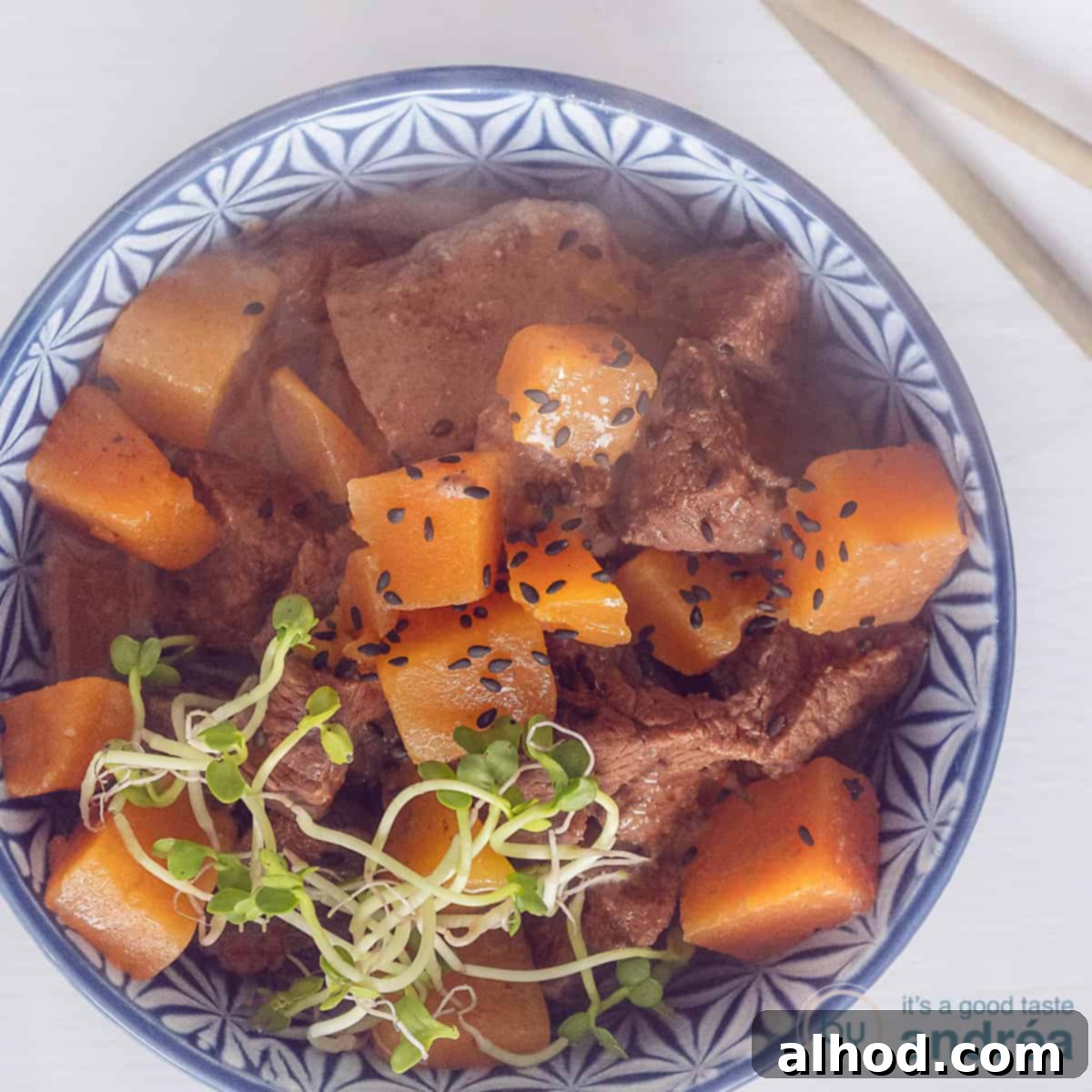 Speedy Rich Beef and Pumpkin Curry 4 A square photo of an overhead photo of a blue bowl of steak and pumpkin cubes. Two chopsticks, gold, next to it on the left