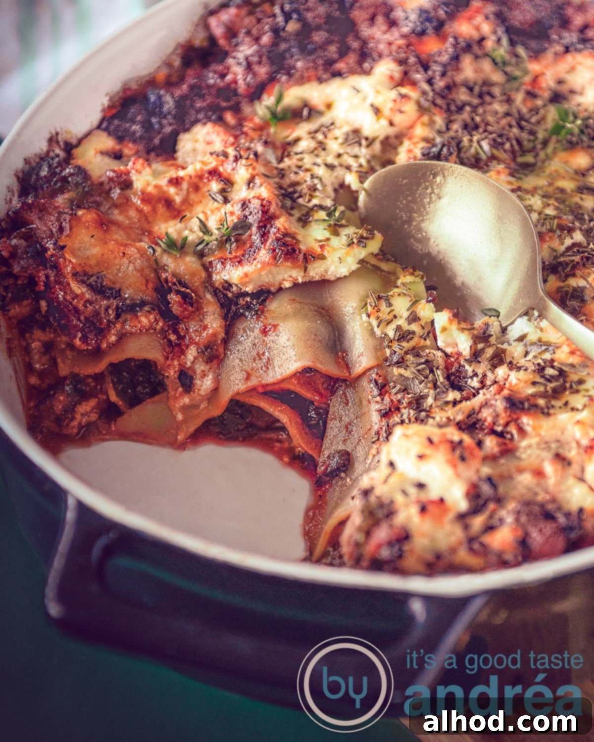 Part of a baking dish filled with kale lasagna, fresh sausage and cheese, garnished with fresh herbs.