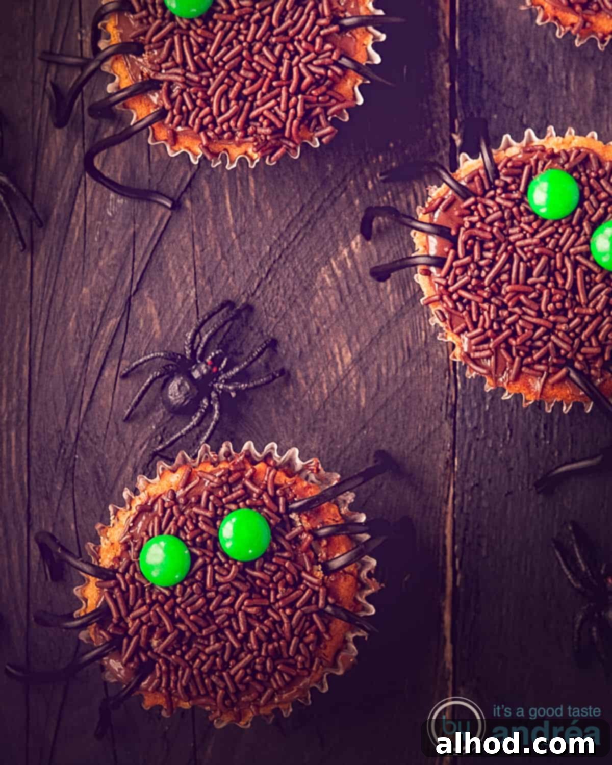 Creepy-Crawly Licorice Leg Cupcakes 4 Çikolata, M&M'ler ve meyan kökü bacakları ile süslenmiş üç adet kapkek, kahverengi bir arka plan üzerinde.