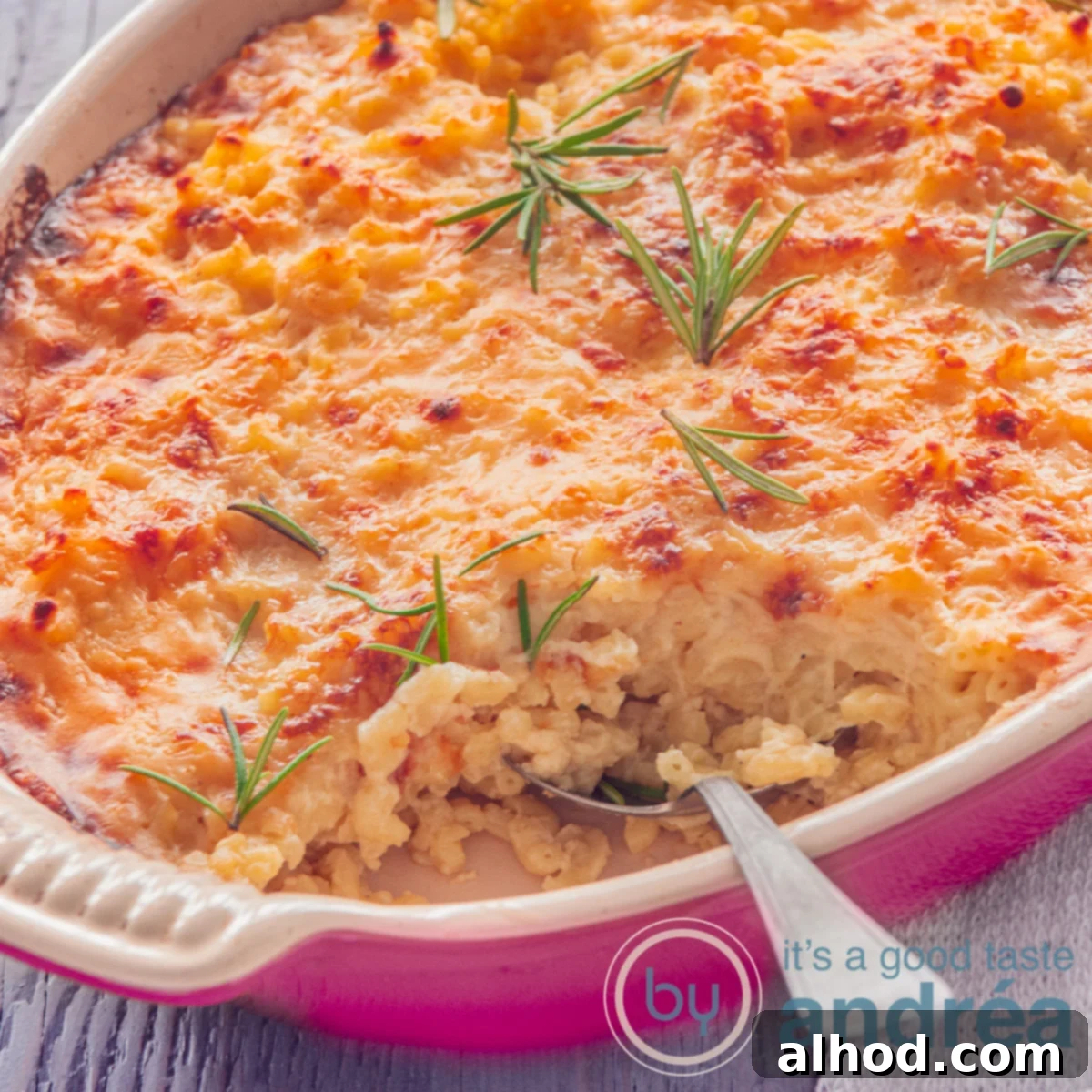 Homestyle Baked Mac and Cheese 4 A square photo with part of a pink baking dish filled with macaroni and cheese, topped with sprigs of rosemary. A spoon sticks in. A gray background.
