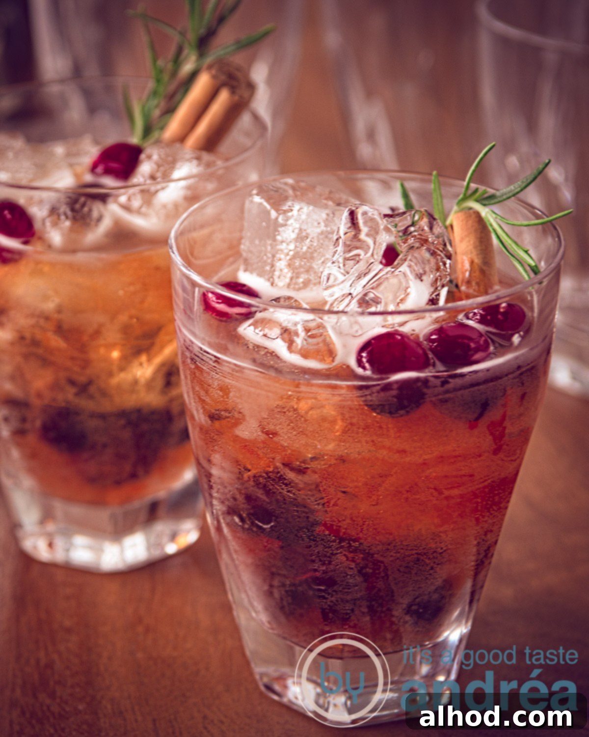 Thanksgiving Cranberry Sparkler 5 Two cranberry cocktail placed behind each other on a wooden table. Decorated with a cinnamon stick, cranberries and a rosemary twig