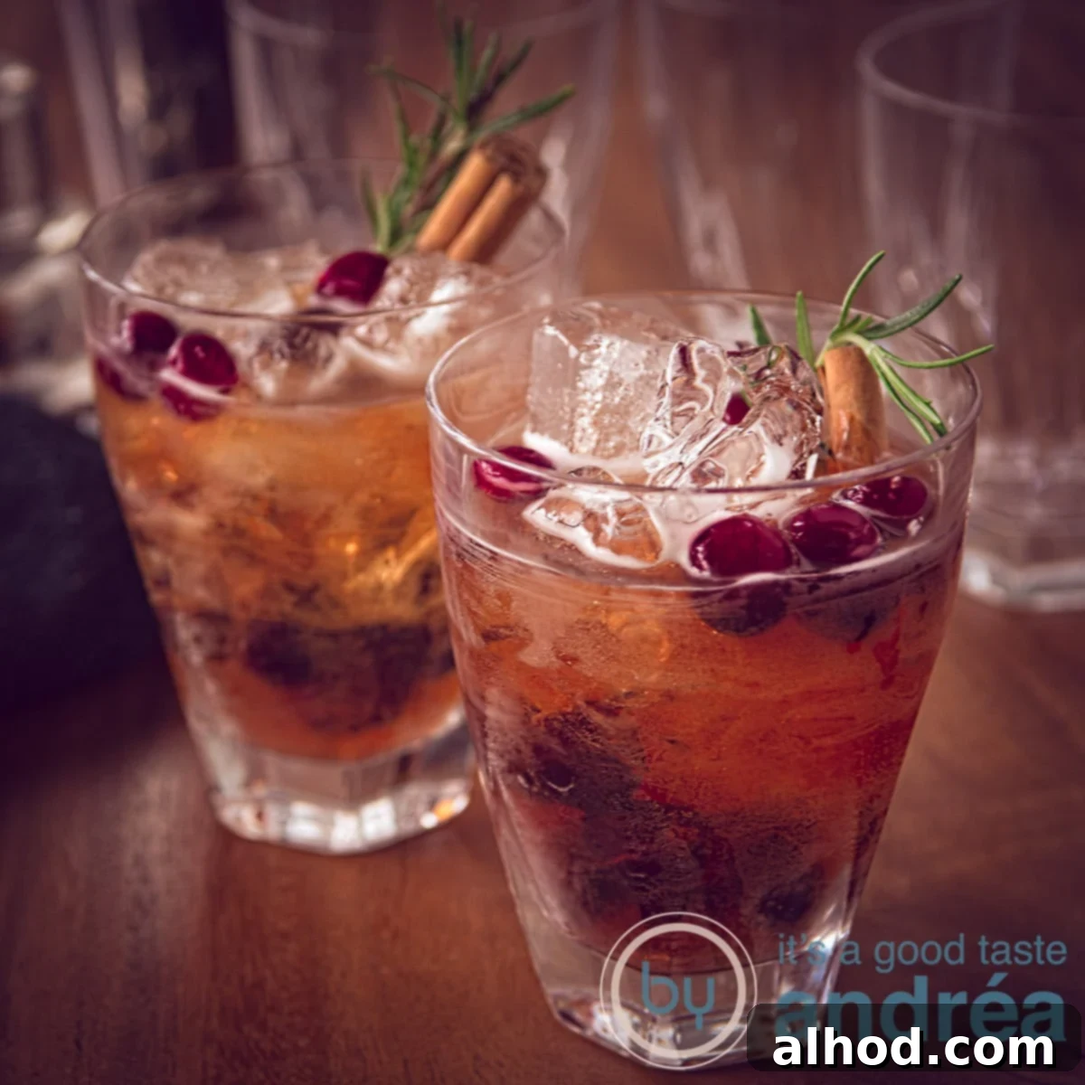 Thanksgiving Cranberry Sparkler 6 A square photo with two glasses filled with a Prosecco cranberry cocktail diagonally behind each other. With ice cream, cinnamon and rosemary. A wooden tabletop