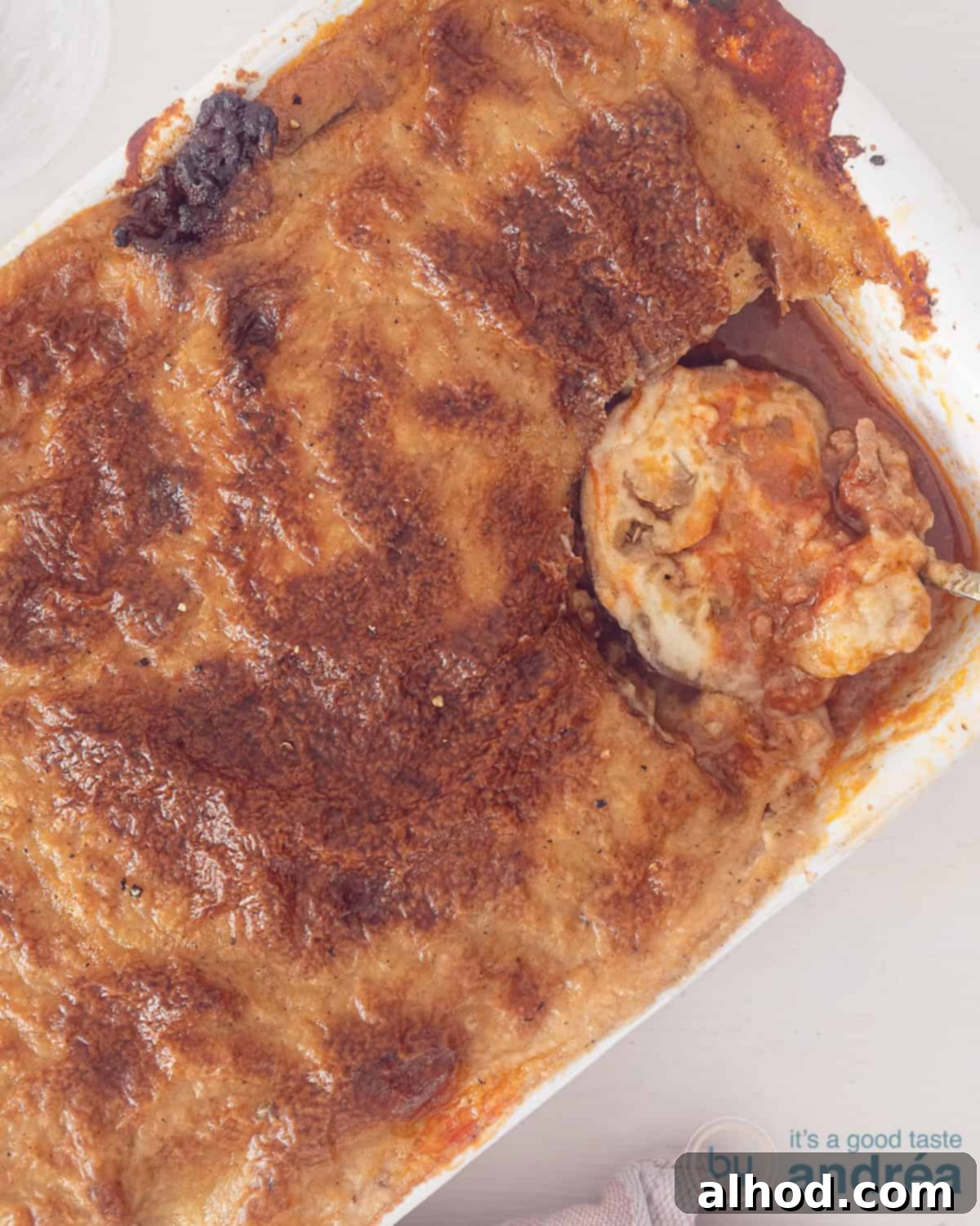 Authentic Greek Eggplant Moussaka Bake 2 A photo from above of a white baking dish with Greek Moussaka from which a portion is scooped.
