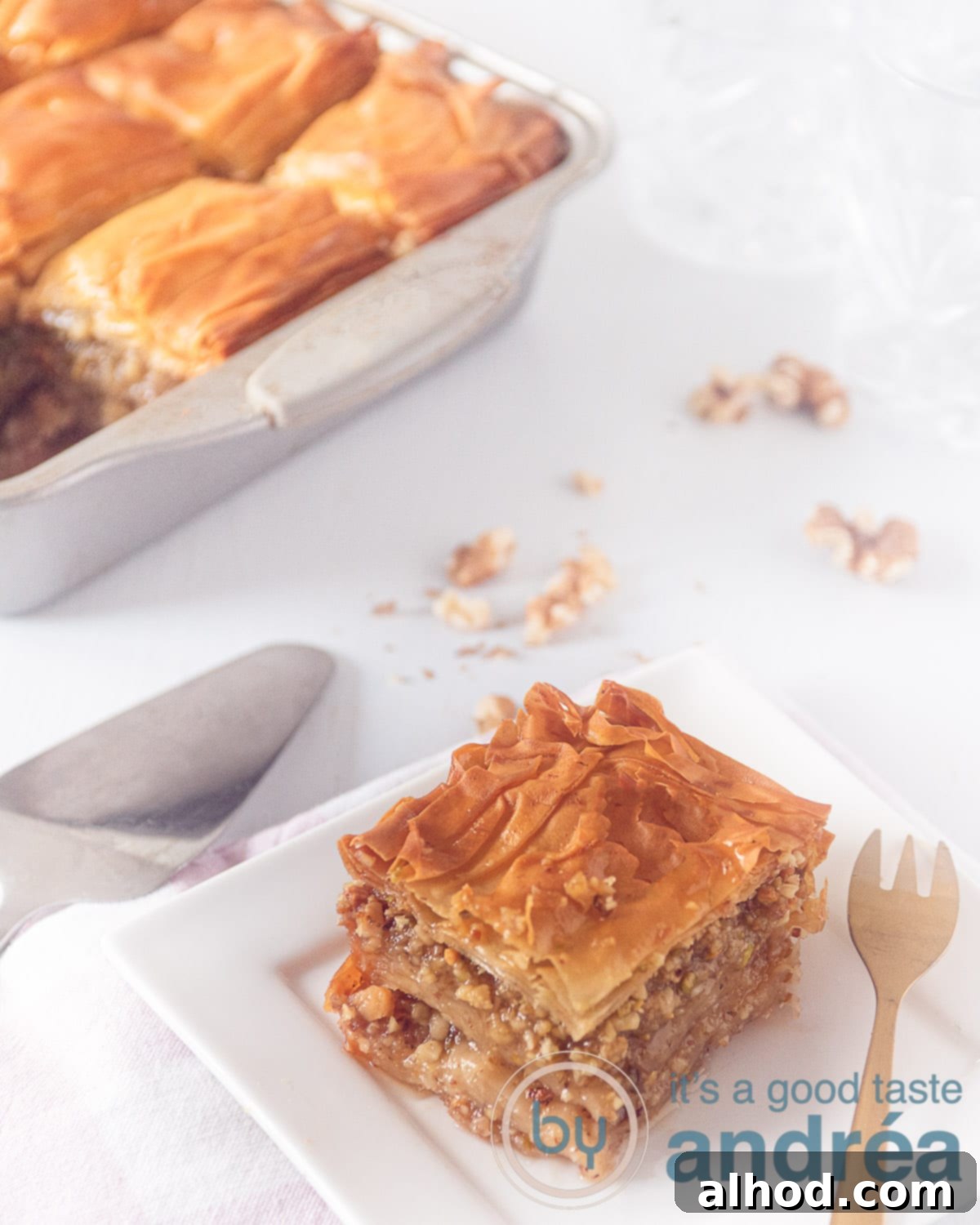 Sweet Greek Baklava Walnut Honey Perfection 2 Deliciously golden Greek Baklava with walnuts and honey, a single piece served on a white plate with a golden fork, and a baking dish filled with more baklava in the background.