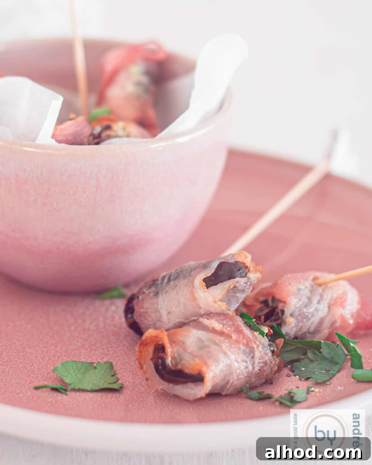 Blue Cheese-Stuffed Bacon-Wrapped Dates 2 A bowl filled with dates and three dates, filled with cheese and wrapped in bacon are in front of it.