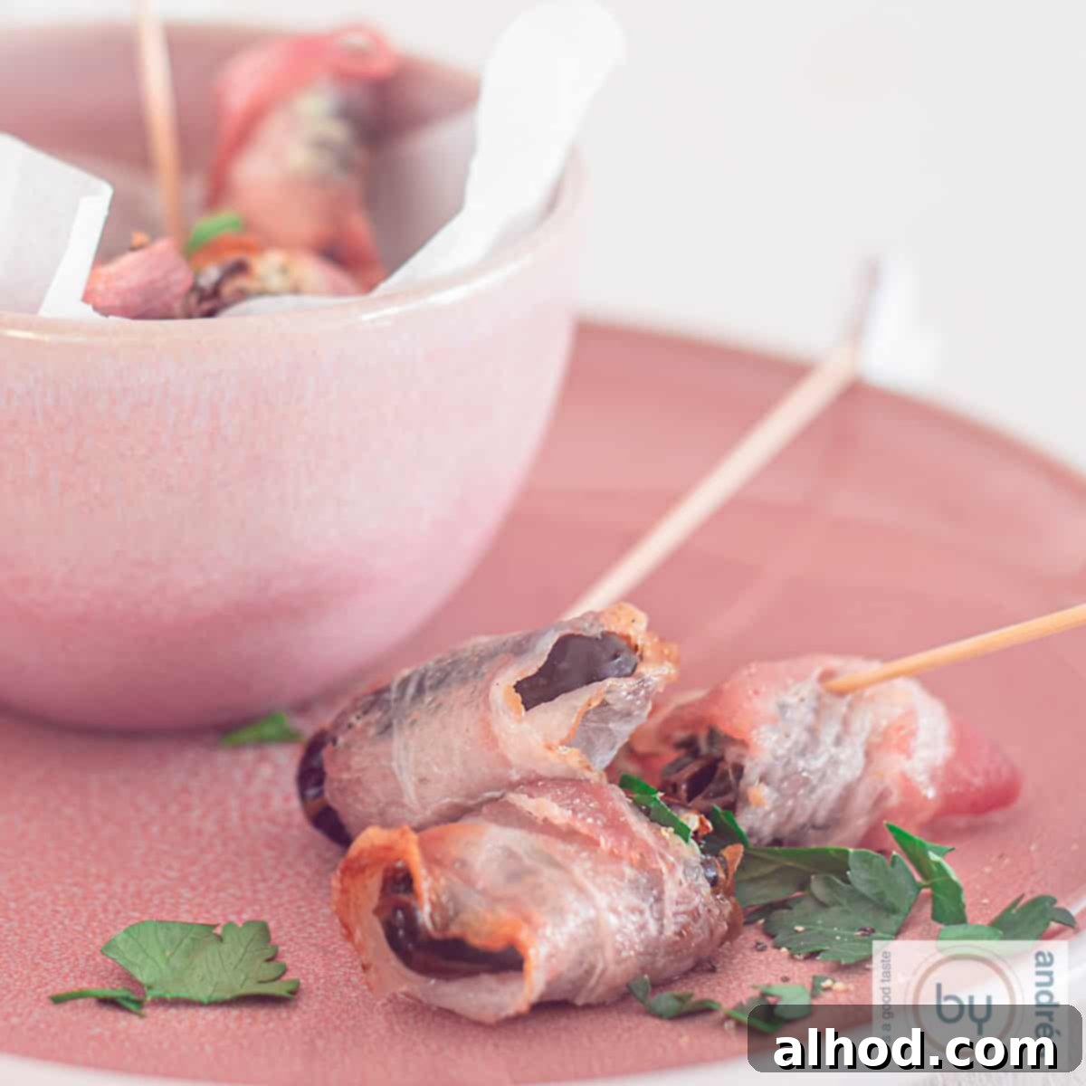 Blue Cheese-Stuffed Bacon-Wrapped Dates 4 A square photo of a pink plate with a bowl filled with dates filled with blue cheese and a bacon wrap