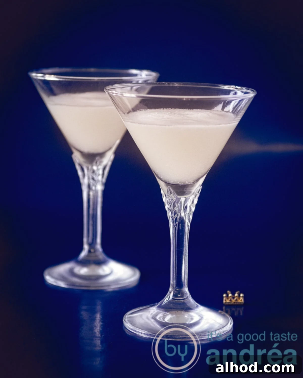 The Perfect Sherry Sour 3 Two elegant crystal glasses filled with creamy Sherry Sour cocktails, beautifully garnished with fresh lemon twists, set against a stylish blue background.